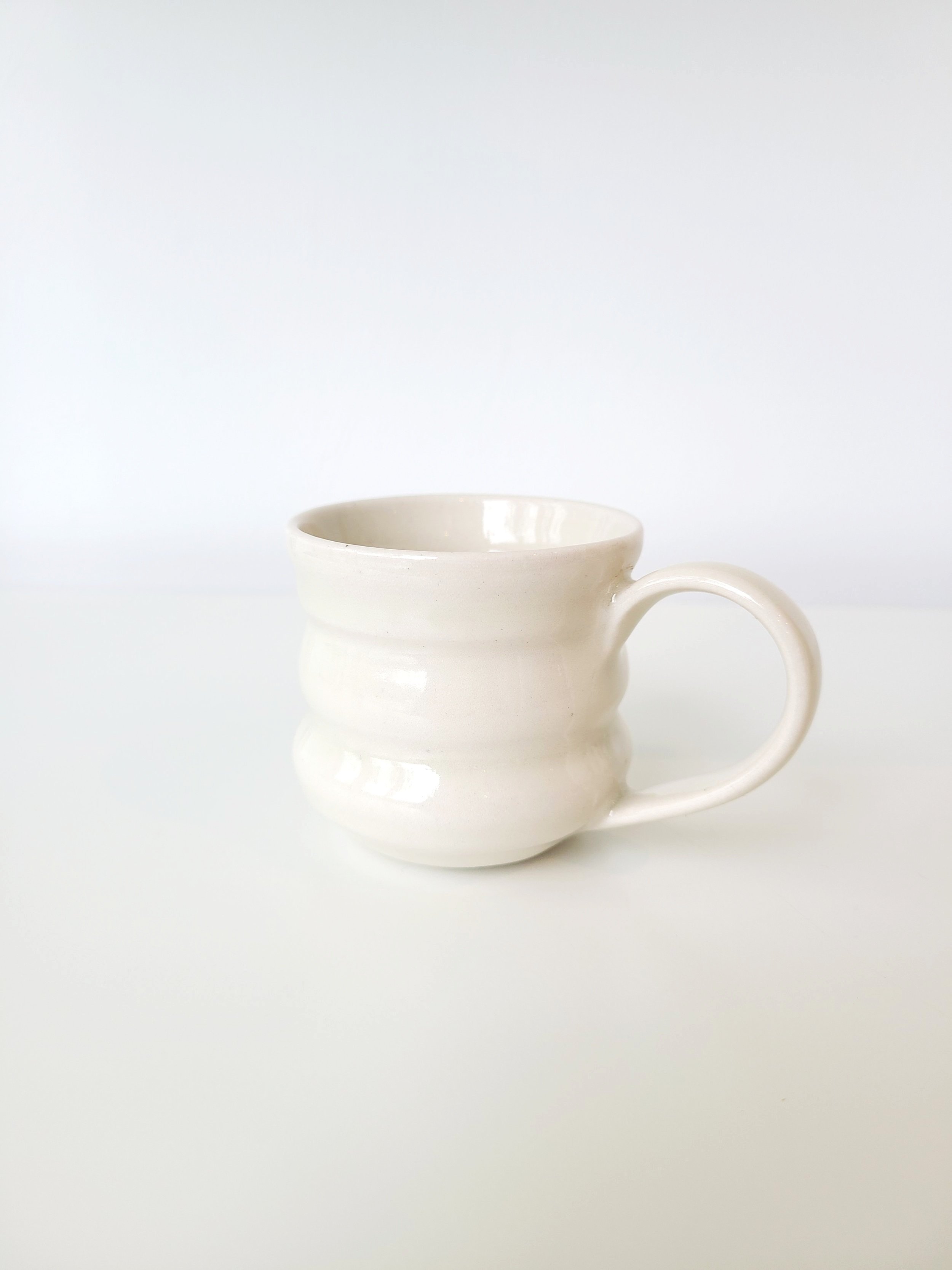 White ceramic mug with a textured, curved design, placed on a white surface against a plain white background.