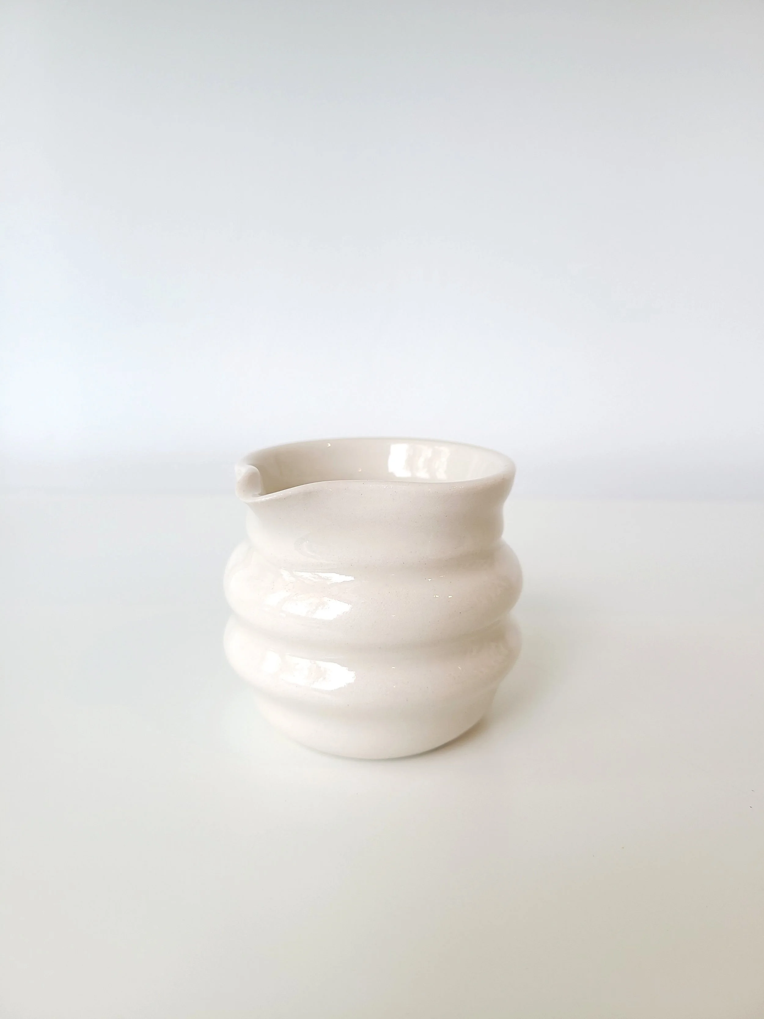 White ceramic cup with a ribbed, wavy design on a white surface against a white background.