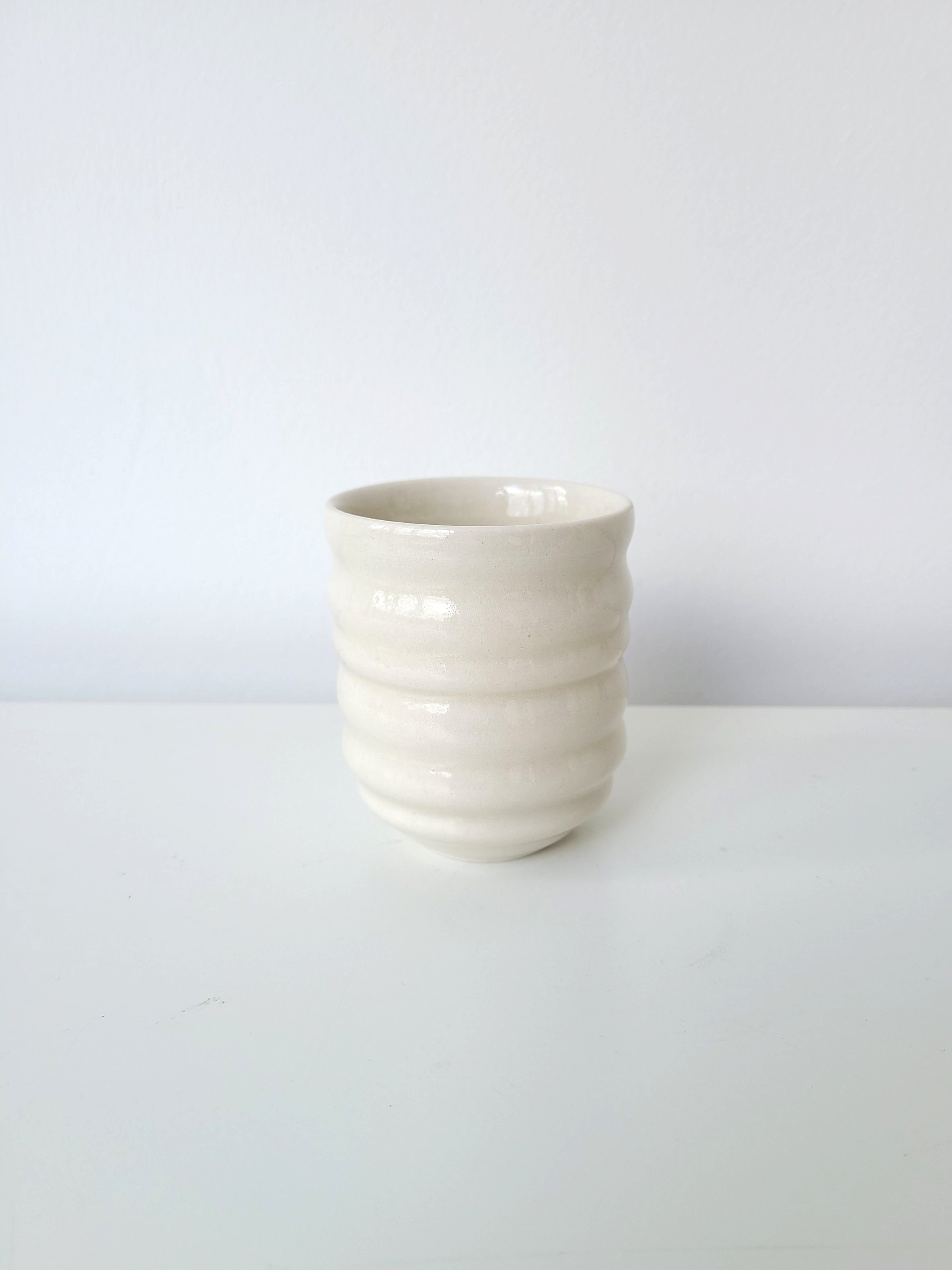 White ceramic cup with a textured, ridged surface on a white surface against a plain white background.