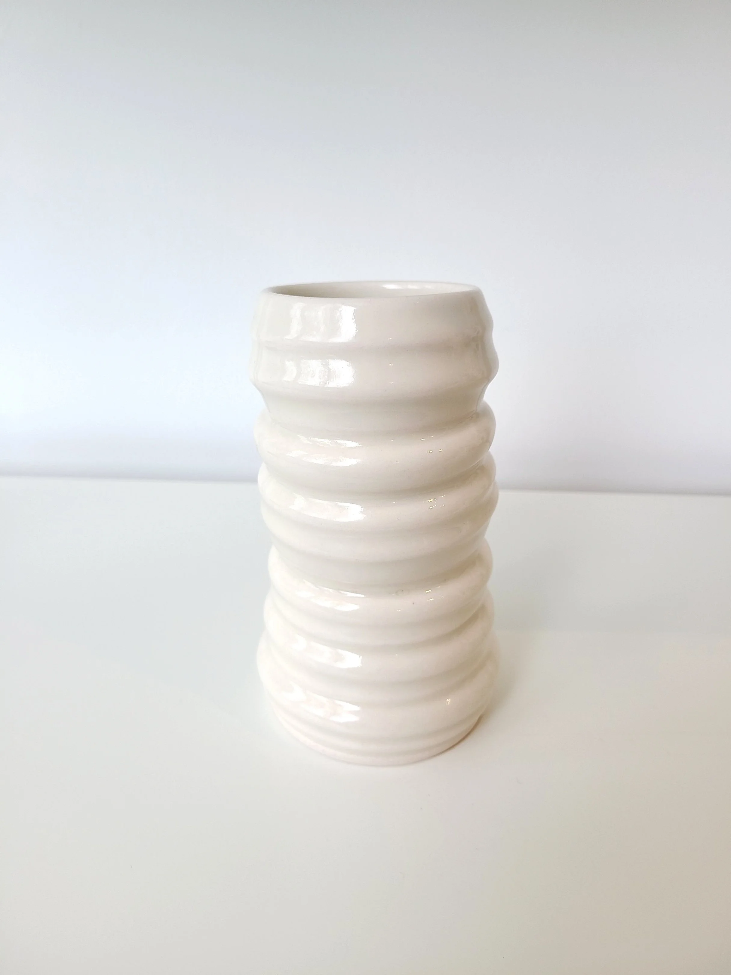 White ceramic ribbed vase on a white surface against a plain white background.