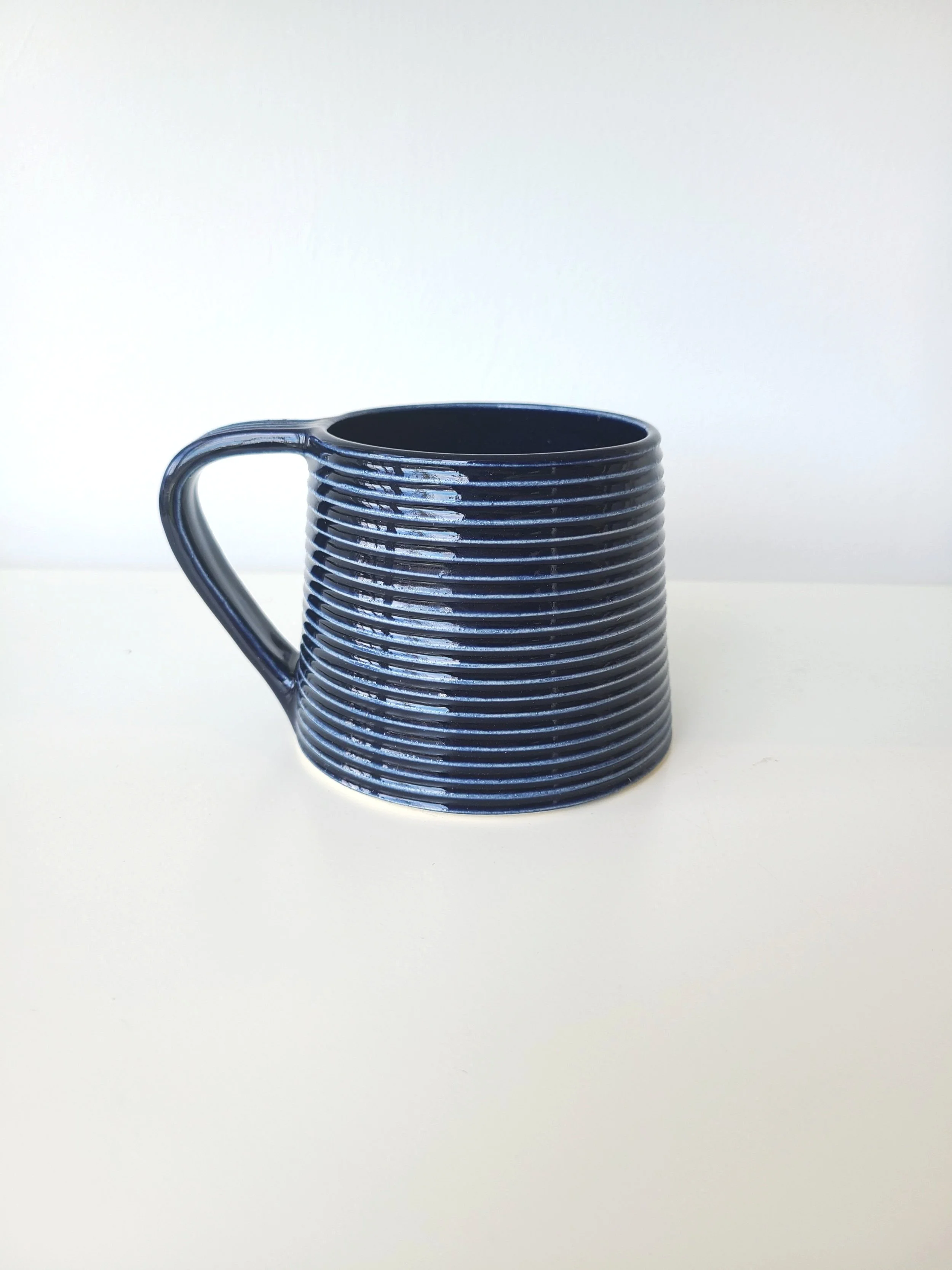 Black ceramic mug with horizontal ridges, placed on a white surface against a light background.