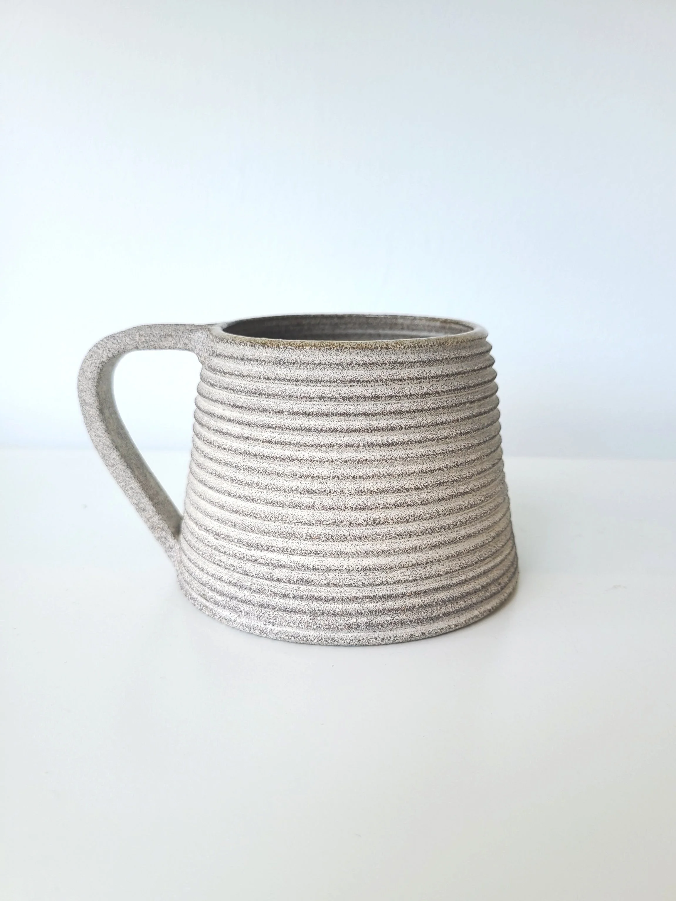 A gray textured ceramic coffee mug with horizontal ridges and a handle, set against a plain white background.
