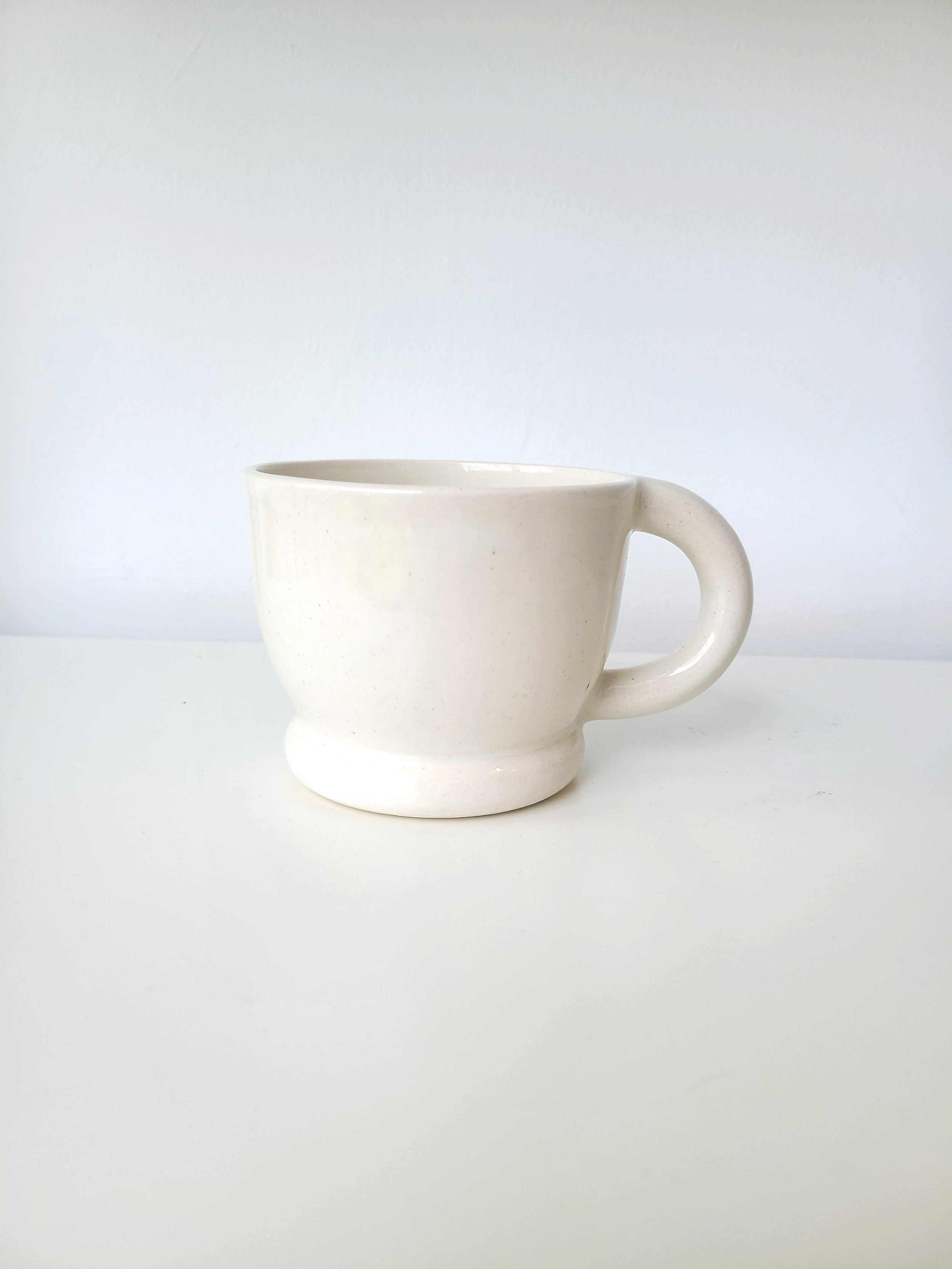 White ceramic coffee mug on a white surface with a plain white background.