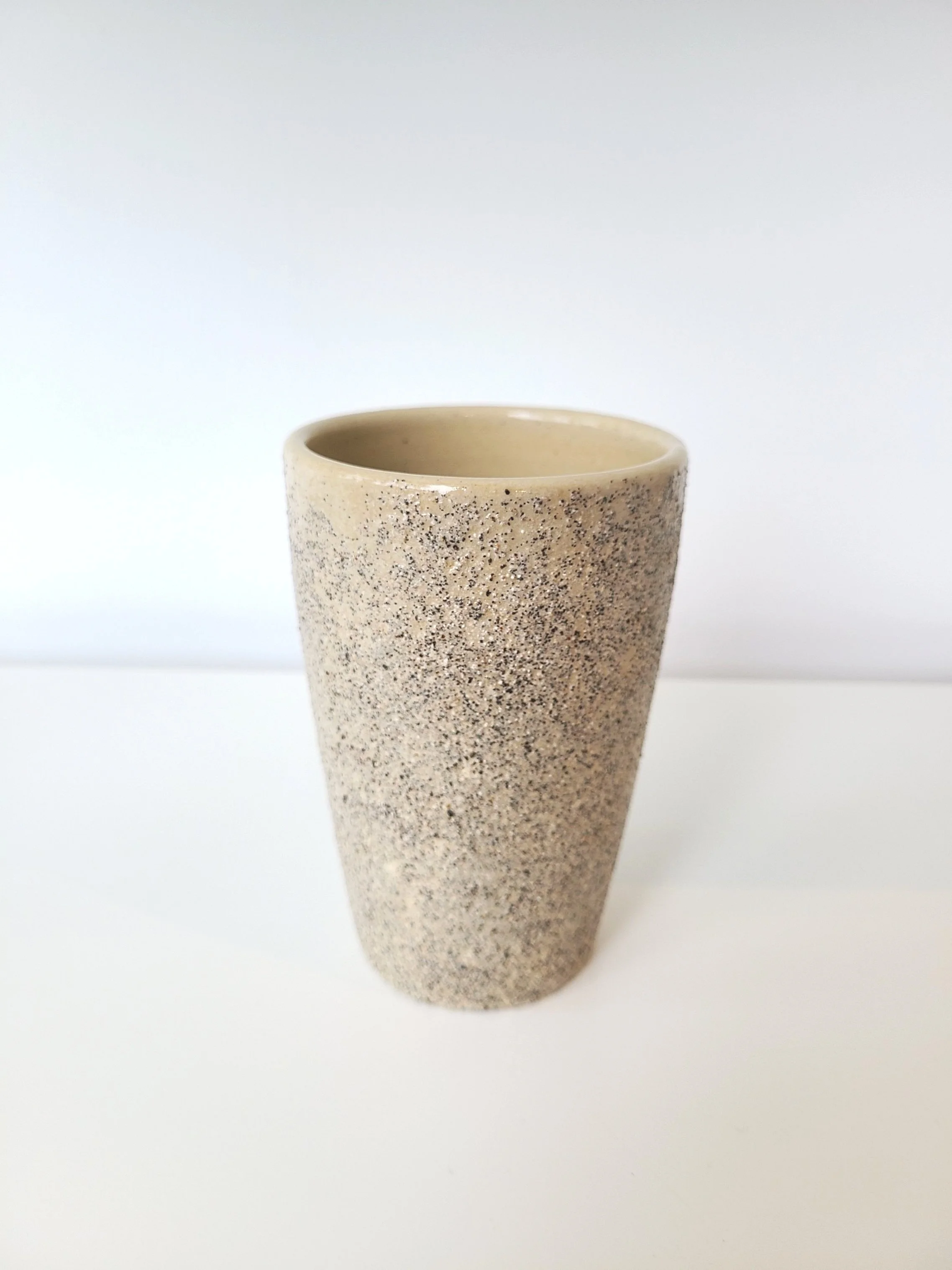 A speckled beige ceramic mug with a smooth interior, set on a white surface against a plain white background.
