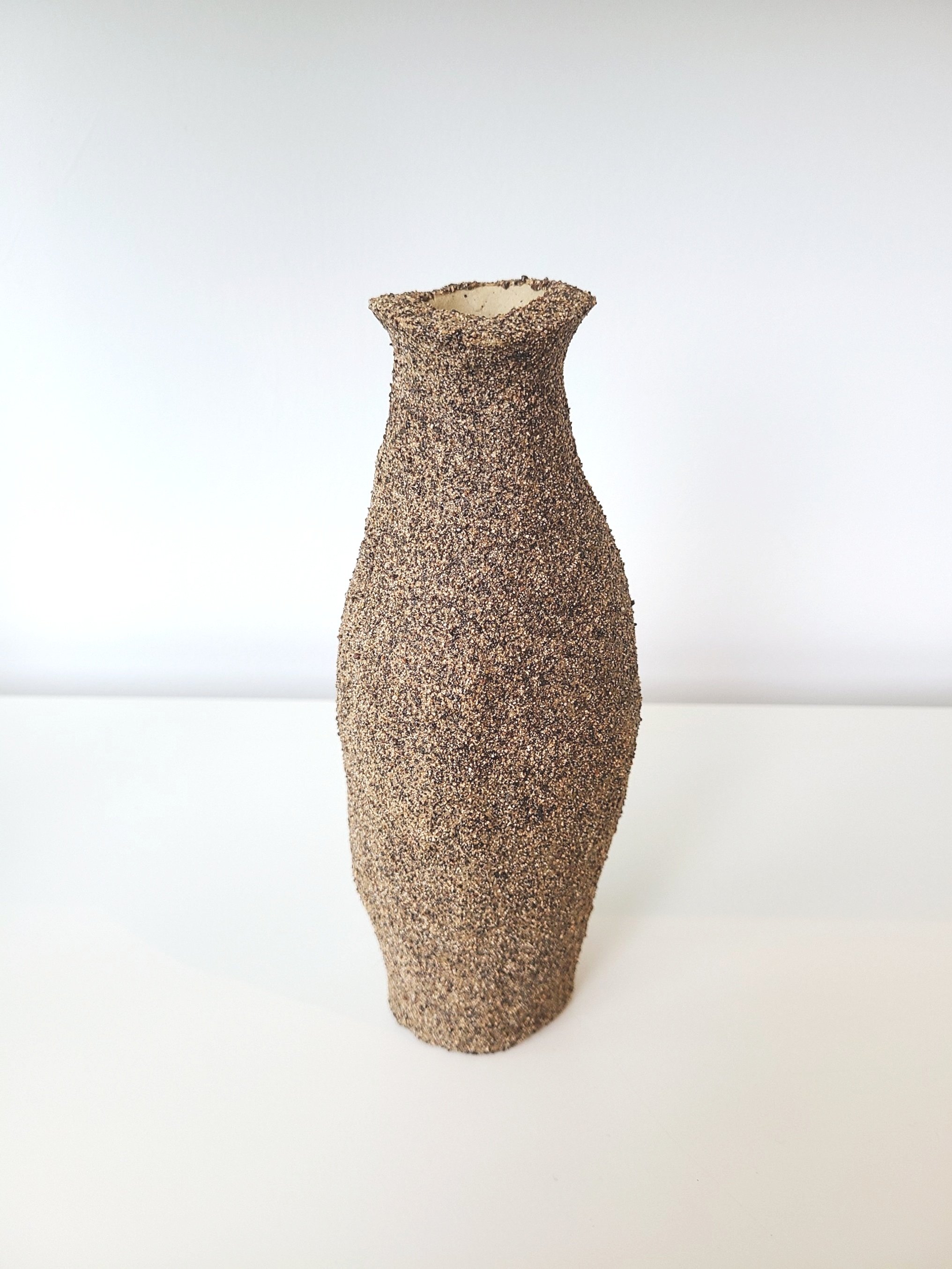 A tall, textured ceramic vase with a narrow neck and flared opening, placed against a plain white background.