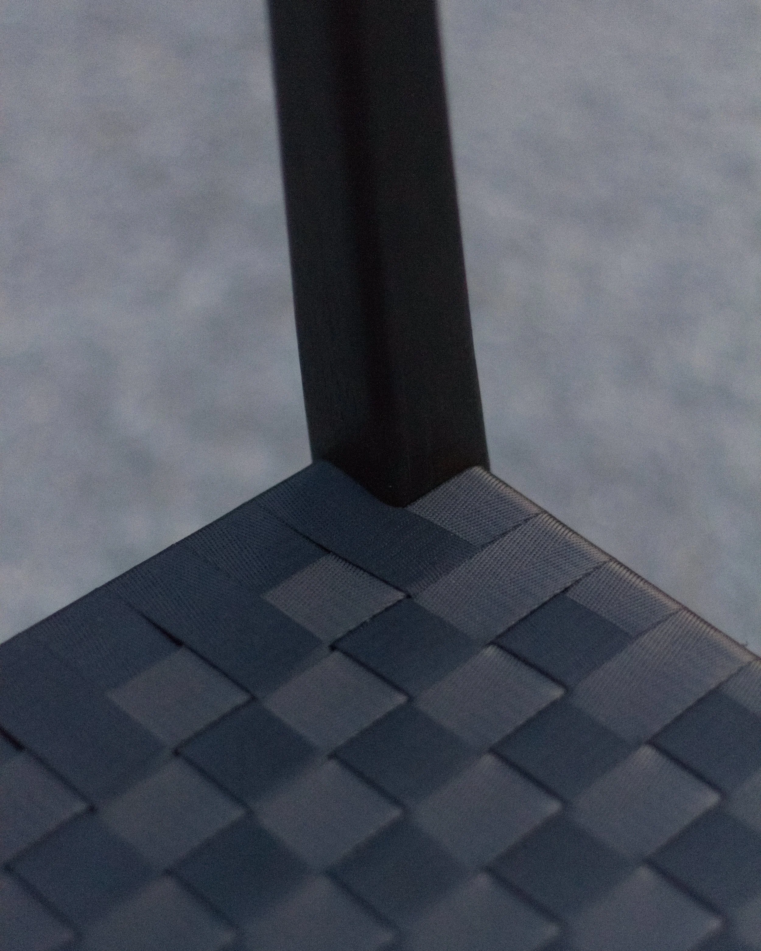 Close-up of a dark, vertical metal pole and horizontal textured surface below it, possibly part of an outdoor structure like a bridge or rail.