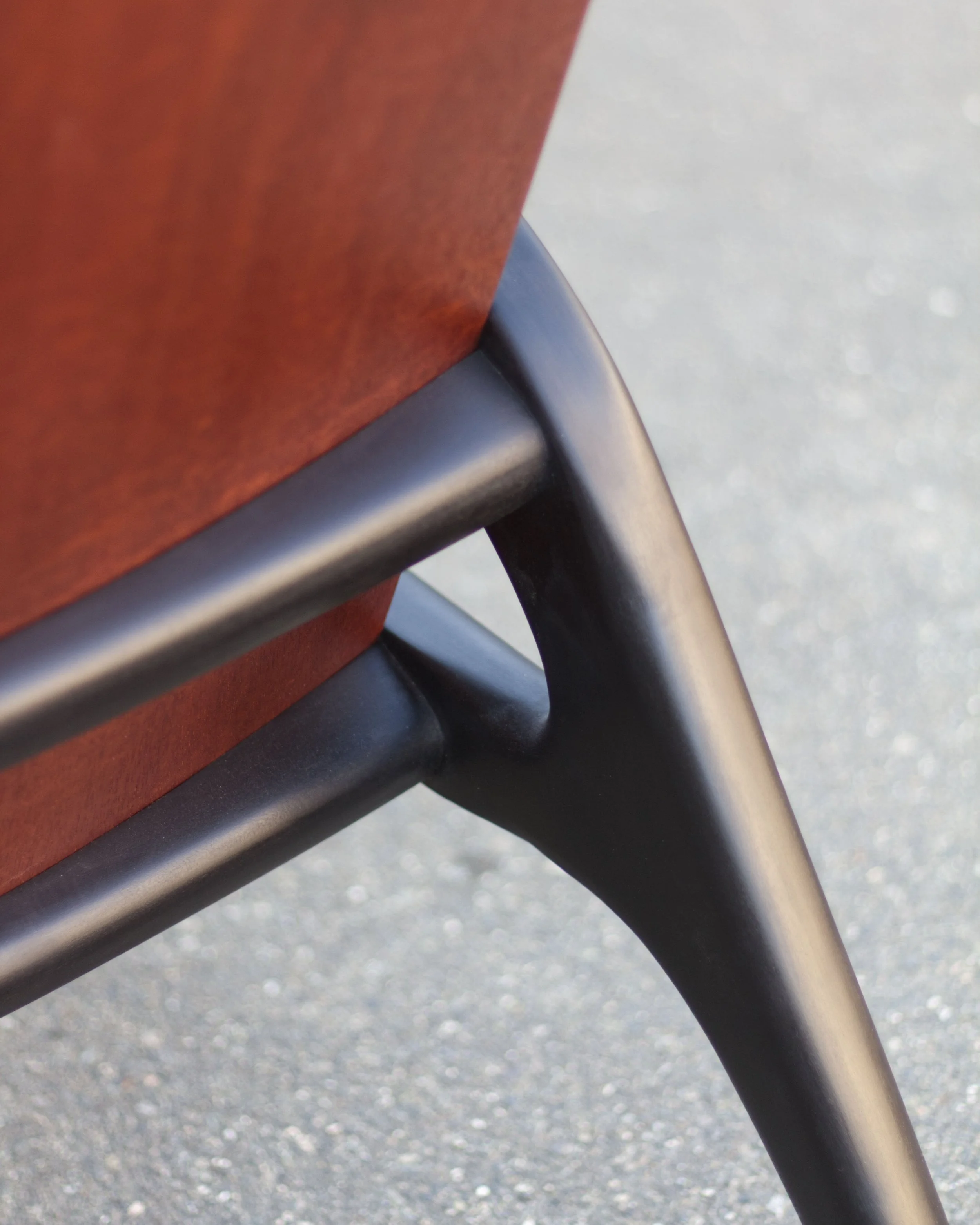 Close-up of a metal chair leg and a wooden slat seat on a pavement surface.