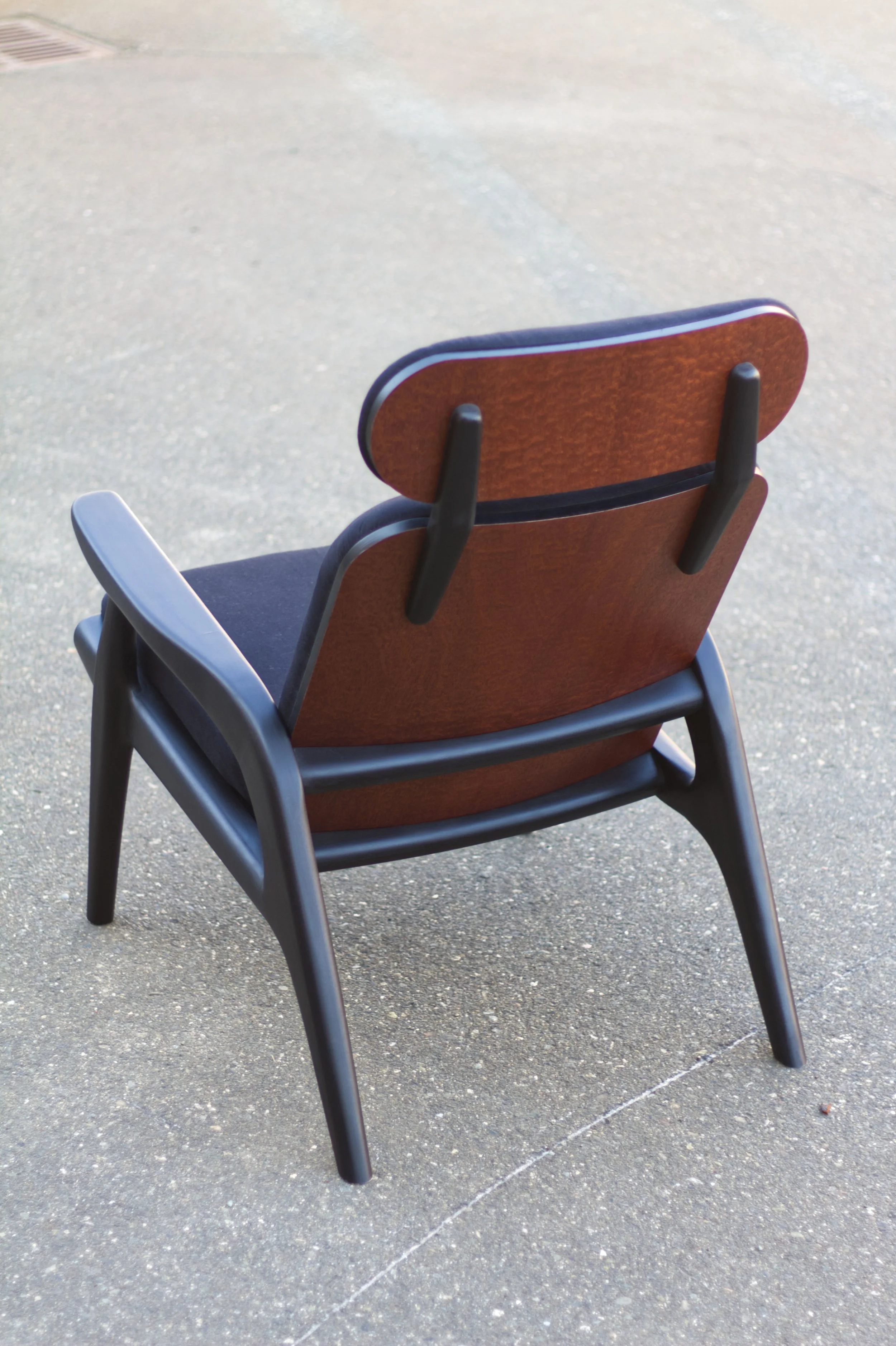 A wooden chair with black armrests, placed on a gray concrete surface outdoors.