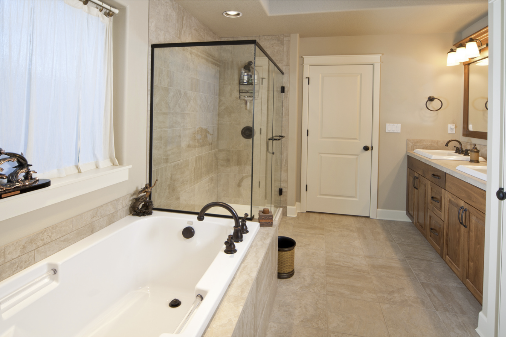 A spacious bathroom with a large bathtub, a walk-in shower with glass enclosure, a double vanity with wooden cabinets and two sinks, a mirror above the vanity, and a window with white curtains.