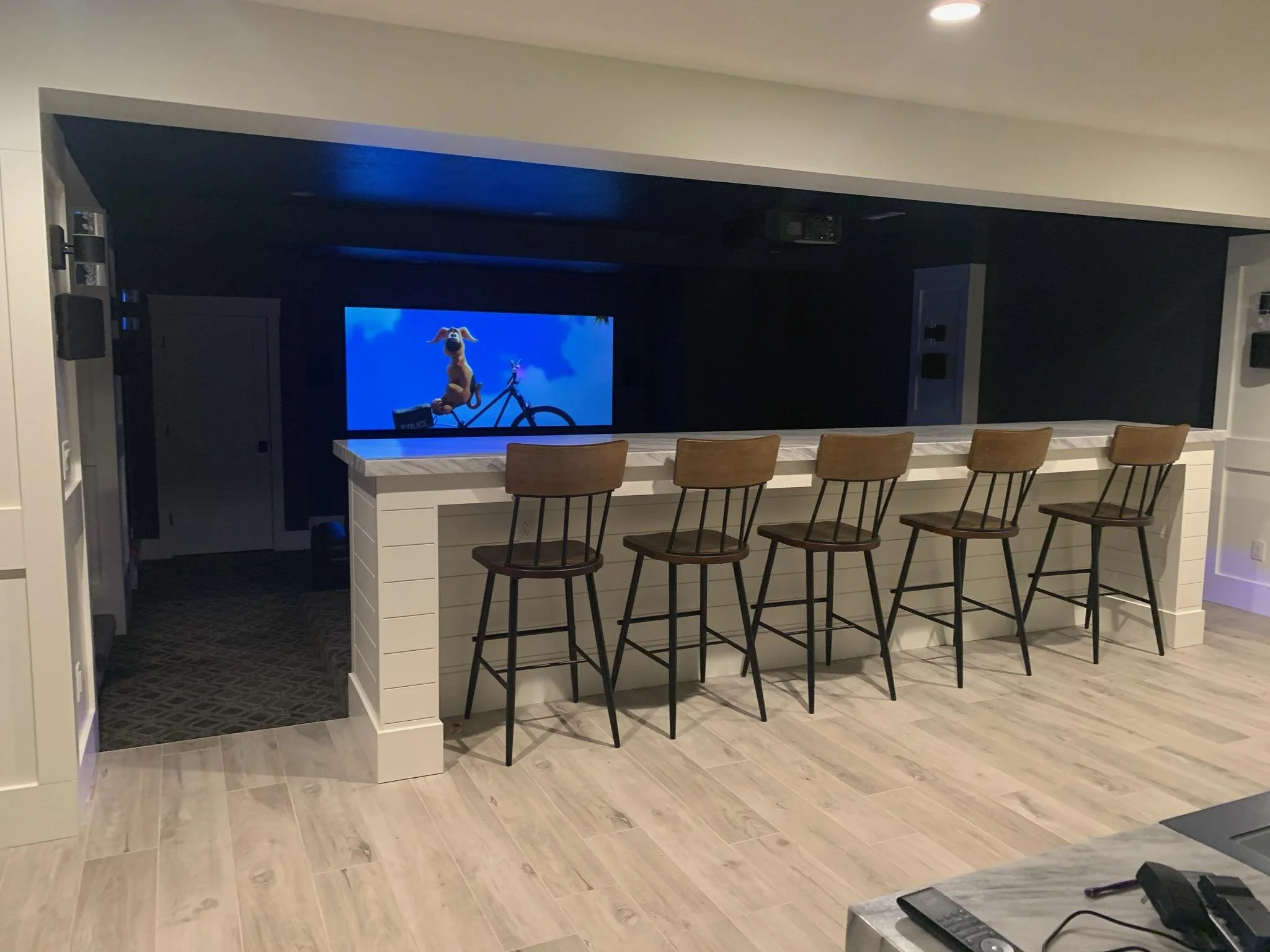A home bar area with five wooden chairs lined up in front of a counter, and a dedicated theater room with projection screen.