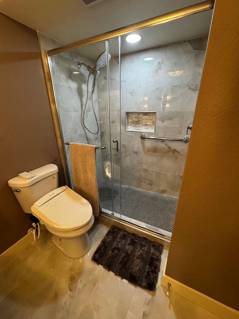 Modern bathroom remodel with a glass shower, marble-style walls, built-in shelf, and updated tile flooring in Tooele Utah