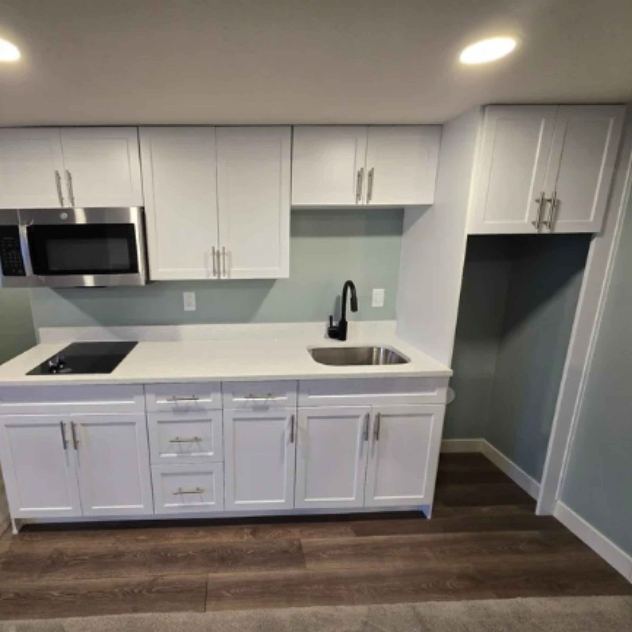 Basement finish with modern white kitchen cabinets, dark wood flooring, stainless steel appliances, and updated finishes in Tooele Utah
