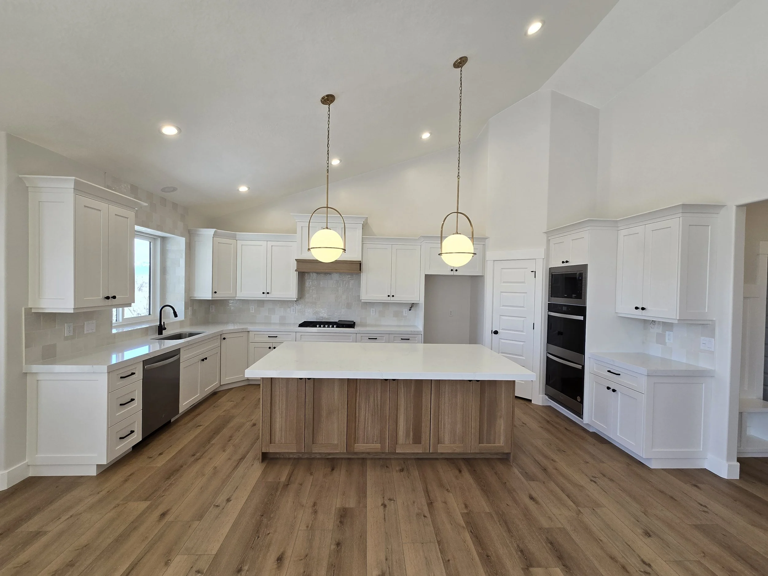 Basement finish with a modern kitchen featuring a custom island, white cabinetry, and upgraded lighting in Tooele Utah