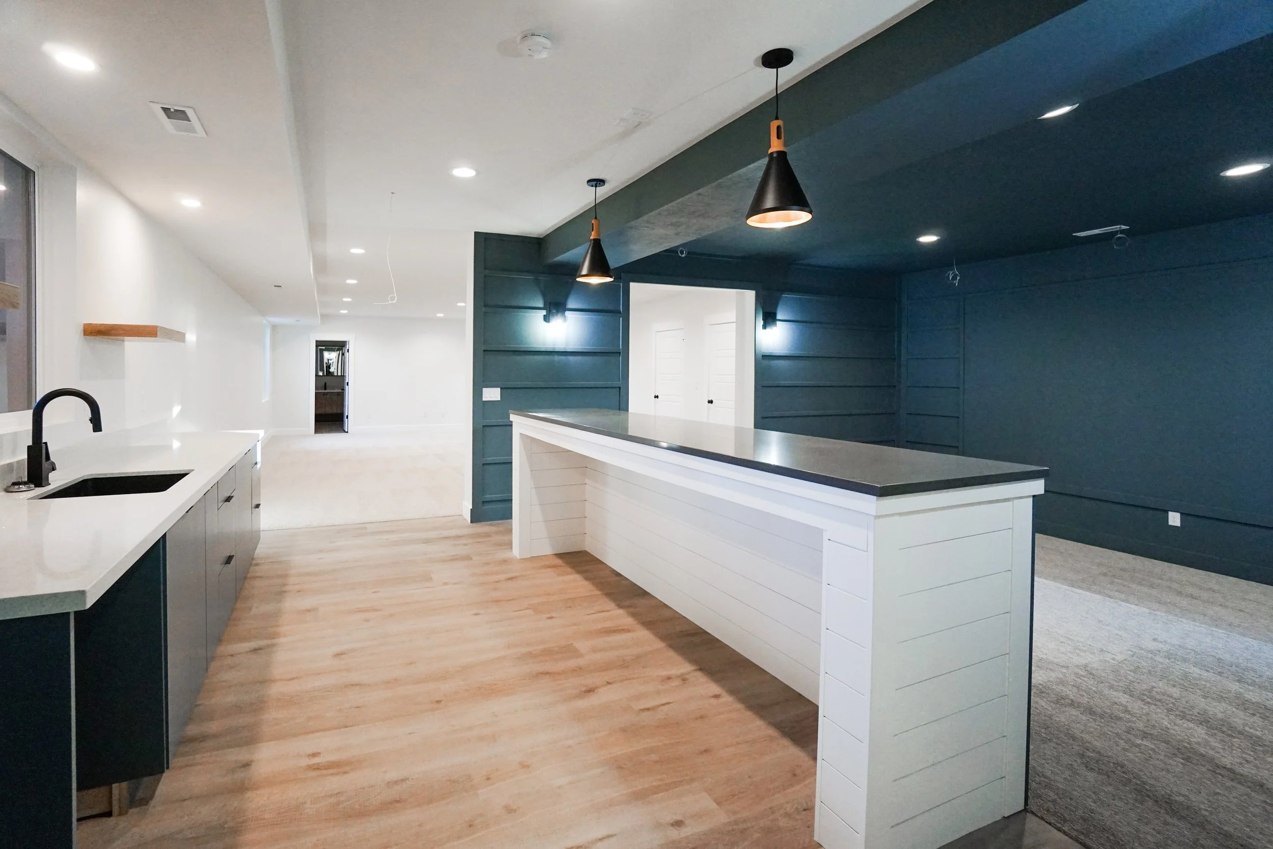 Open-concept kitchen with a white island, dark blue walls, white cabinets, and a light wood floor. Pendant lighting hangs over the island, and recessed ceiling lights are present.