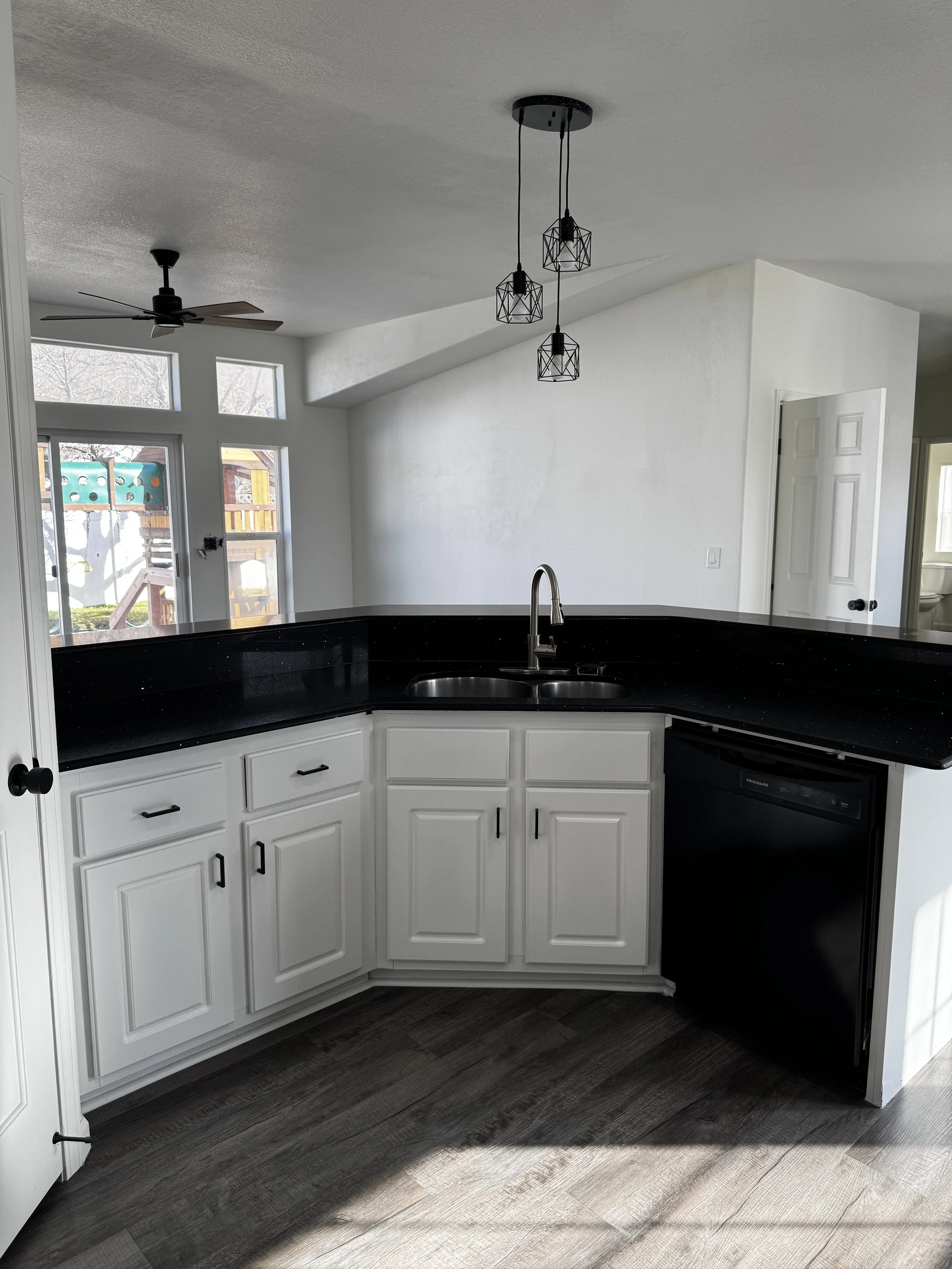 Basement finish with a modern kitchen featuring white cabinets, black countertops, stainless steel appliances, and open layout in Tooele Utah
