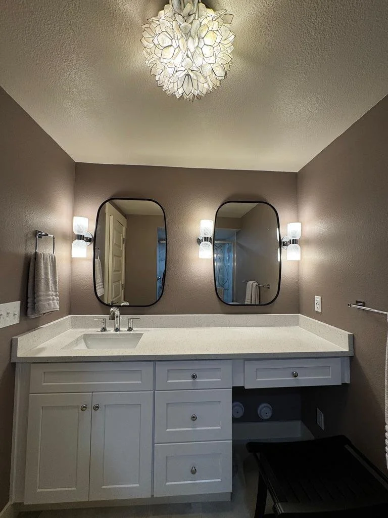 Modern basement bathroom vanity with white countertops, custom cabinetry, updated lighting, and dual mirrors