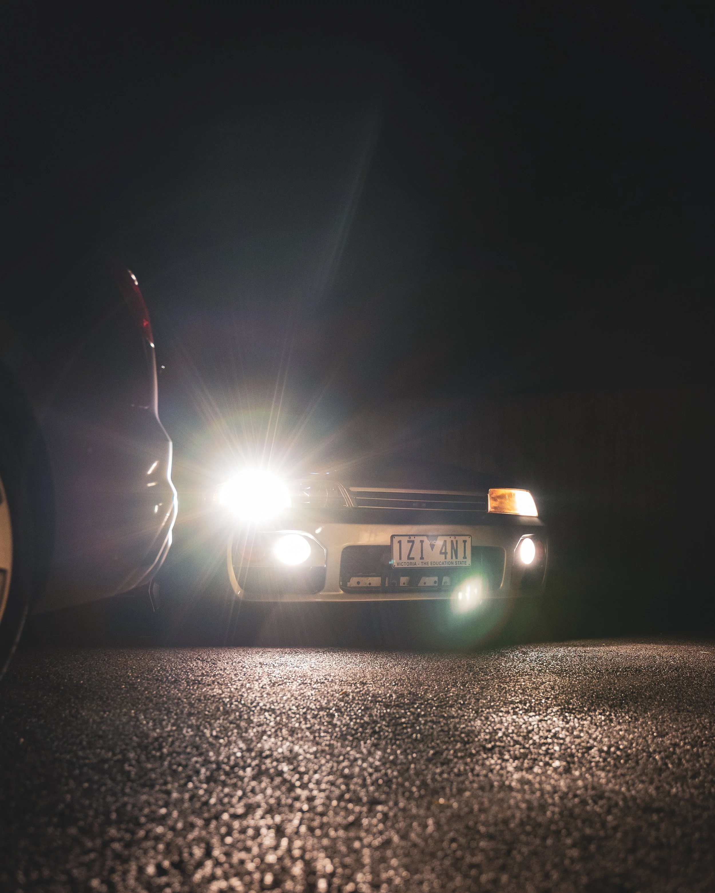 A car with its headlights on parked on a dark street at night, front view with the license plate visible.