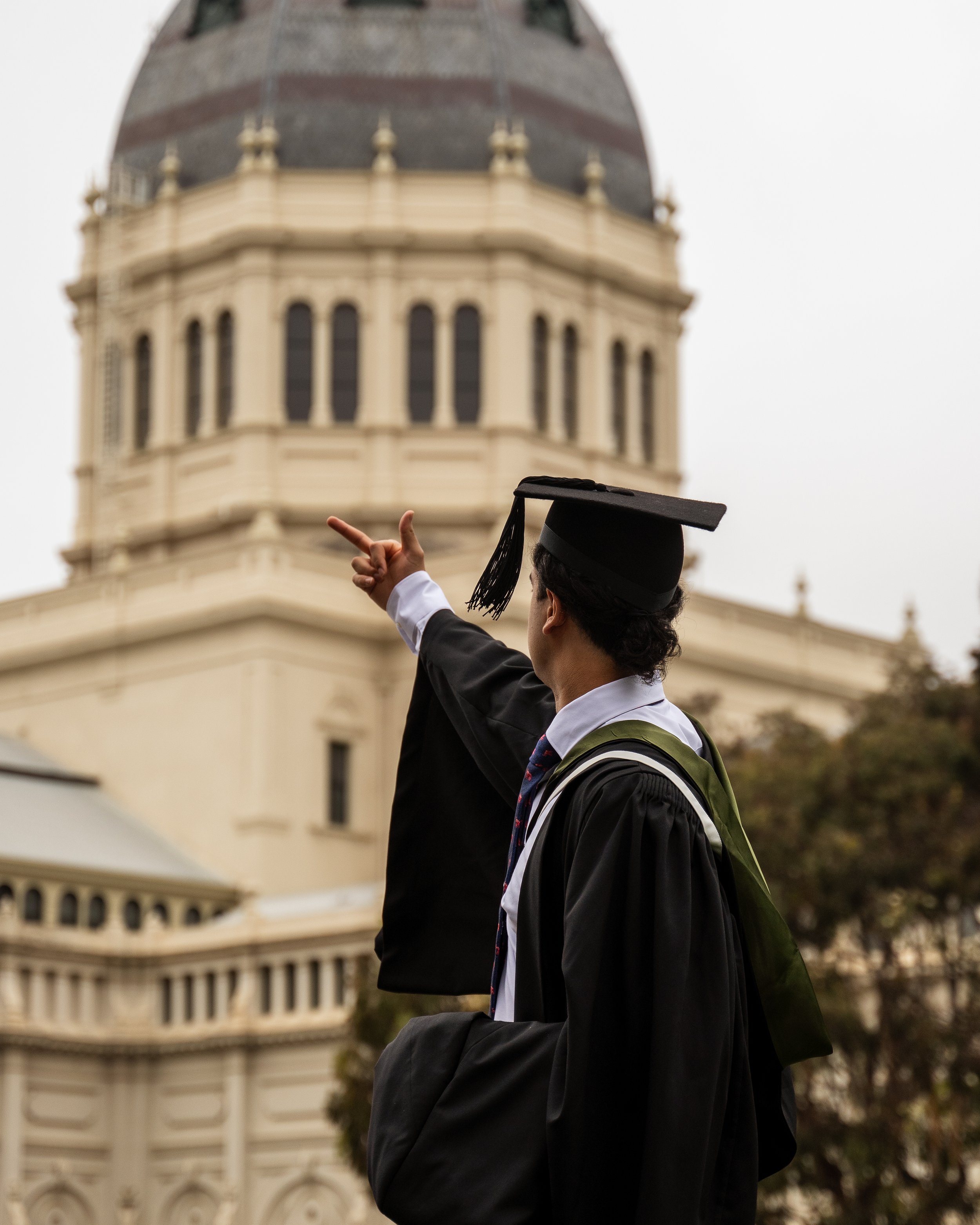 Graduate in cap and gown pointing towards a historic building behind
