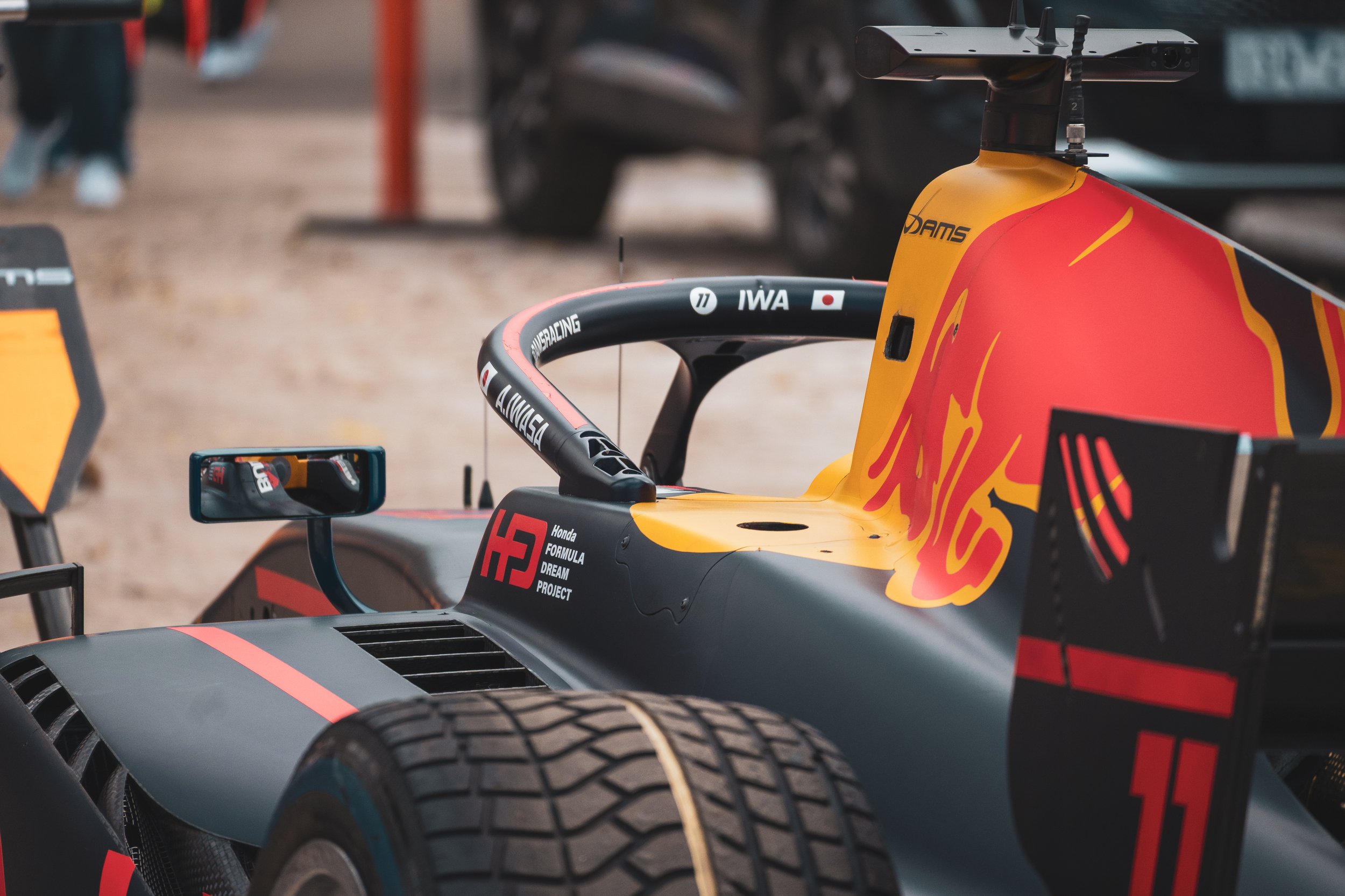 Close-up of a Formula racing car with a red and yellow livery, featuring the Red Bull logo and tires, parked on a dirt surface.