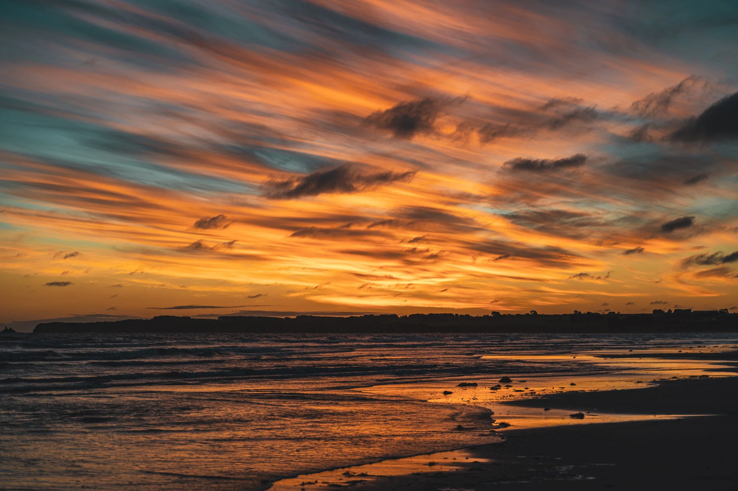 Sunset over the ocean with colorful sky and waves hitting the shore.