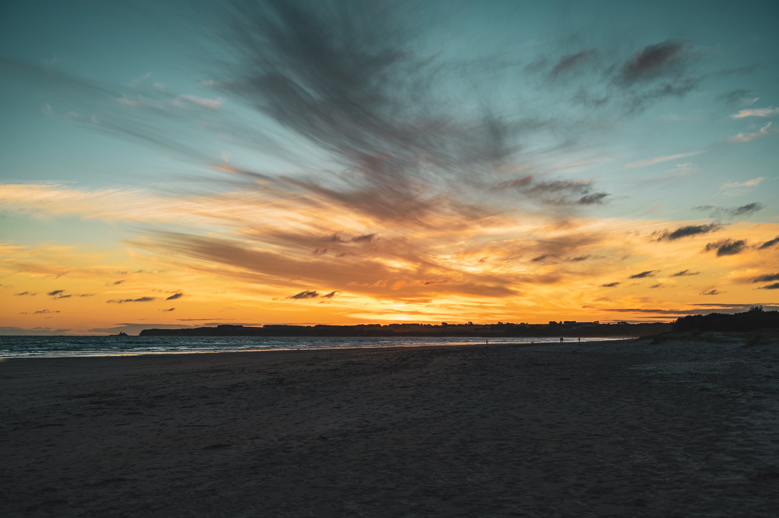 Sunset over the ocean with clouds in the sky and a sandy beach in the foreground.