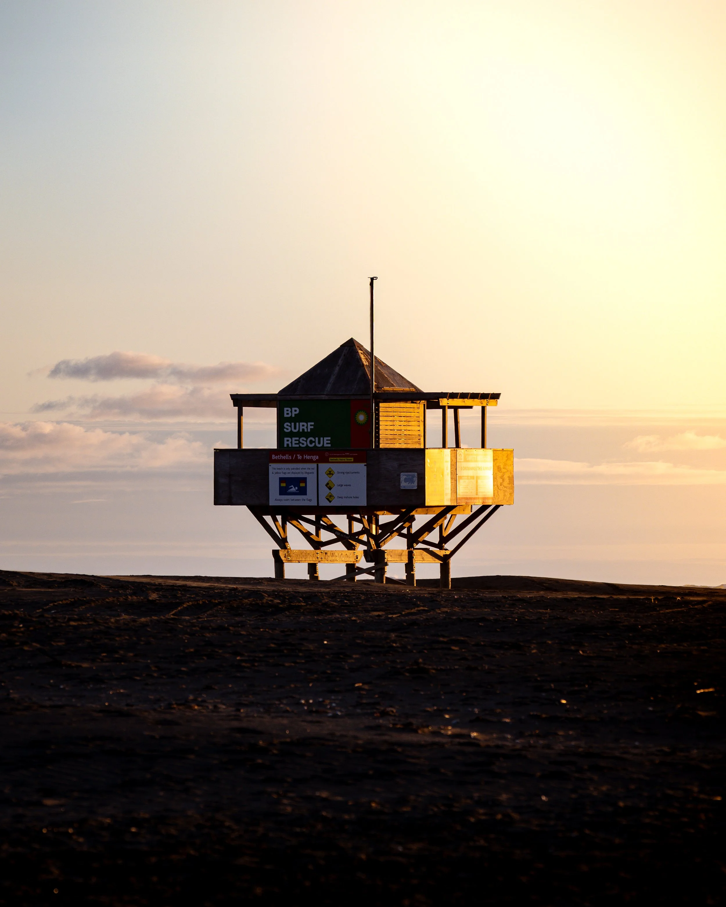 A lifeguard tower on the beach during sunset with a sign that reads 'BP Surf Rescue' and advertisements.