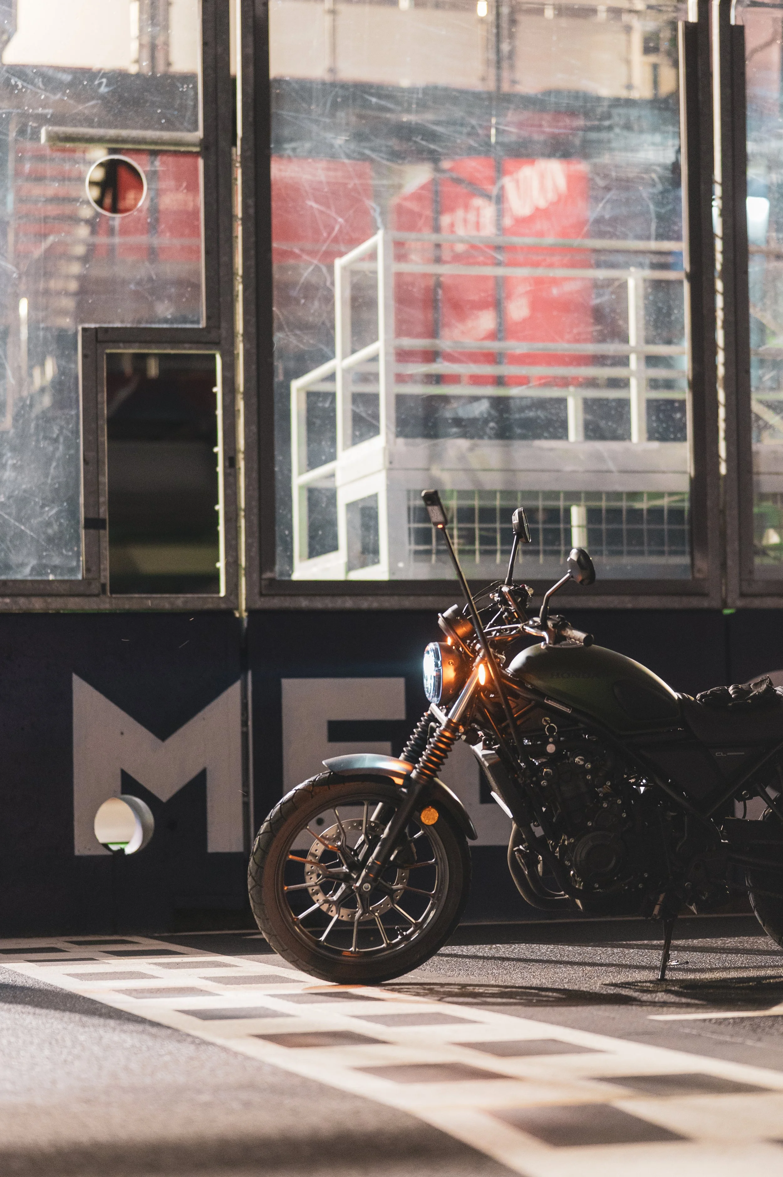 A black motorcycle parked in front of a glass wall with urban reflections at nighttime.