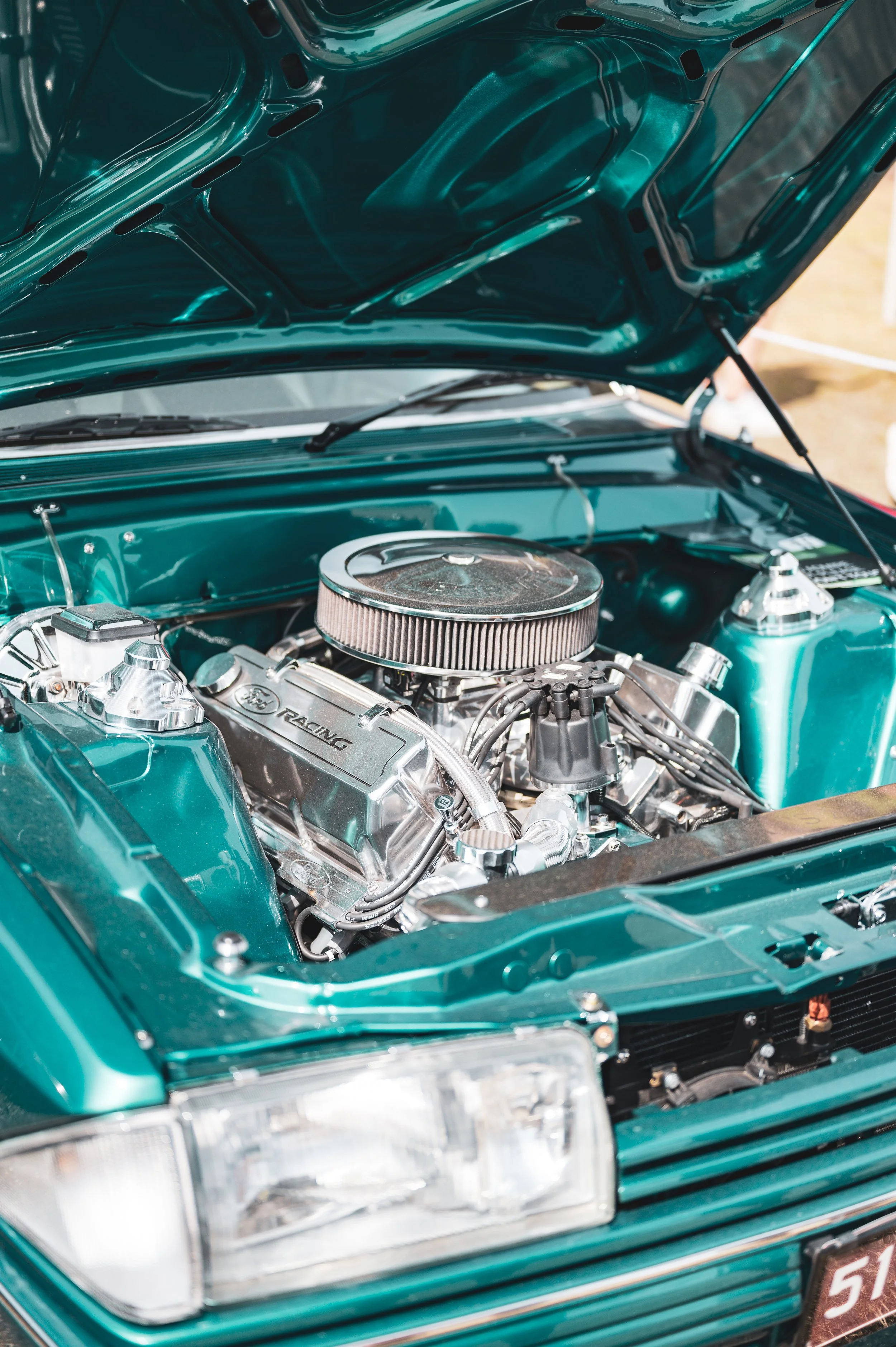 A teal classic car with an open hood revealing a clean, shiny, and well-maintained engine.