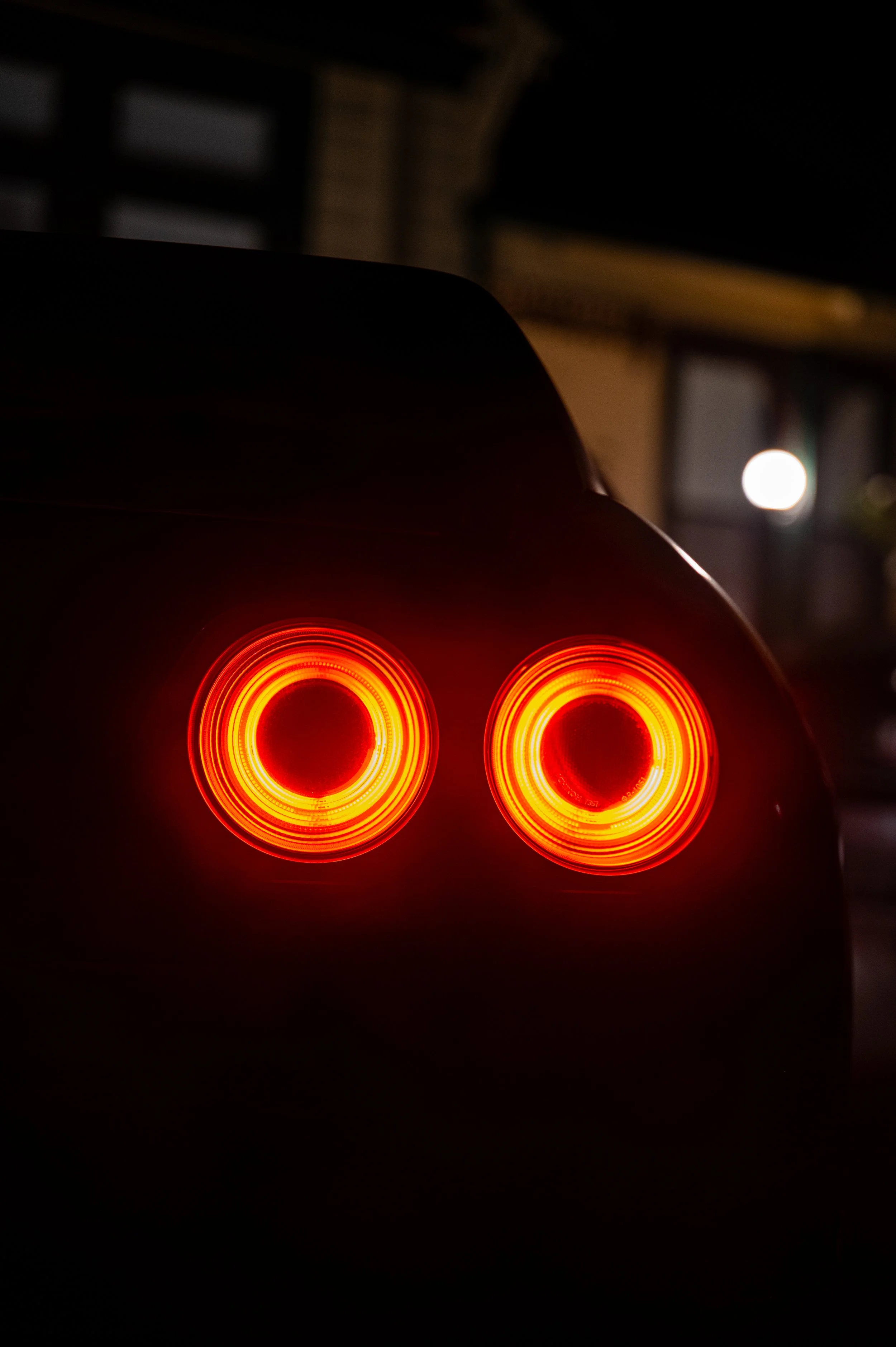 The rear of a car with glowing red circular tail lights at night.