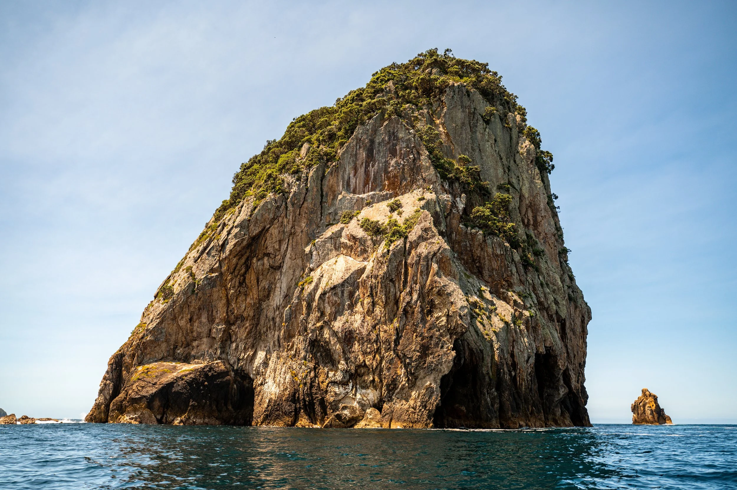 Large rocky island with greenery on top, surrounded by ocean under a blue sky.