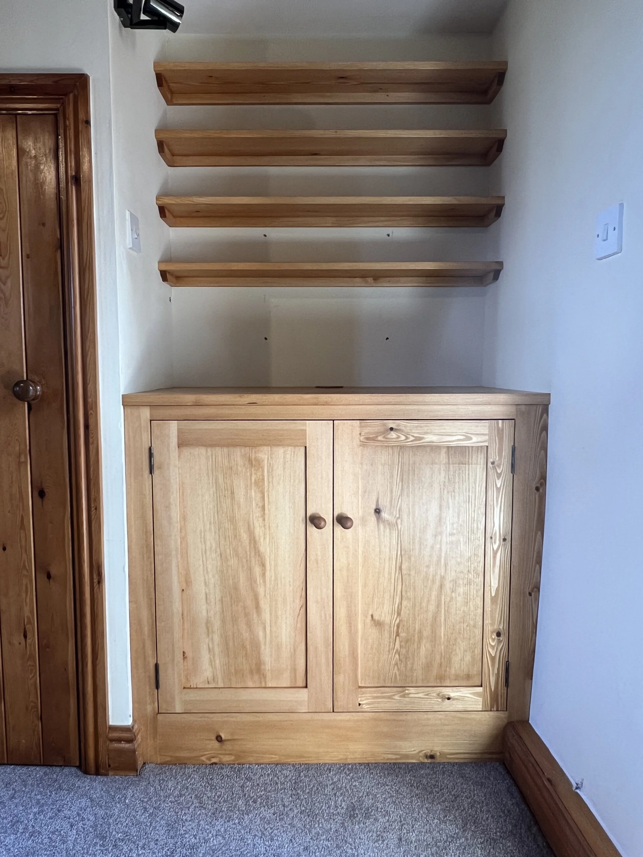 Wooden cabinet with double doors below four floating shelves on a wall in a room.