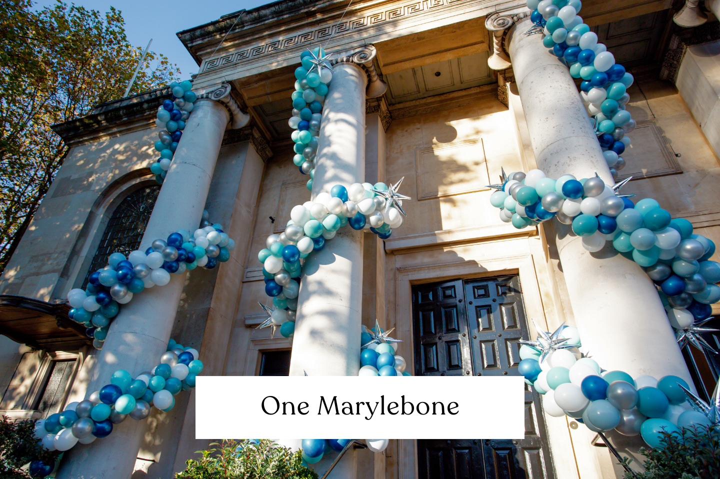 One Marylebone, London. Spiral Garlands in blue, white, silver and gold wrapped around a pillar making a spiral. External balloon garlands wrapping around building. 