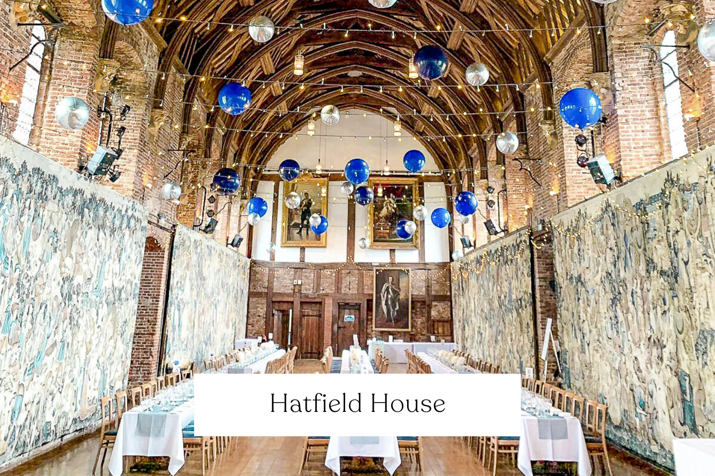 A decorated banquet hall for a wedding. Decorating the space are floating blue and silver balloons suspended between string lights, and artwork on the walls.
