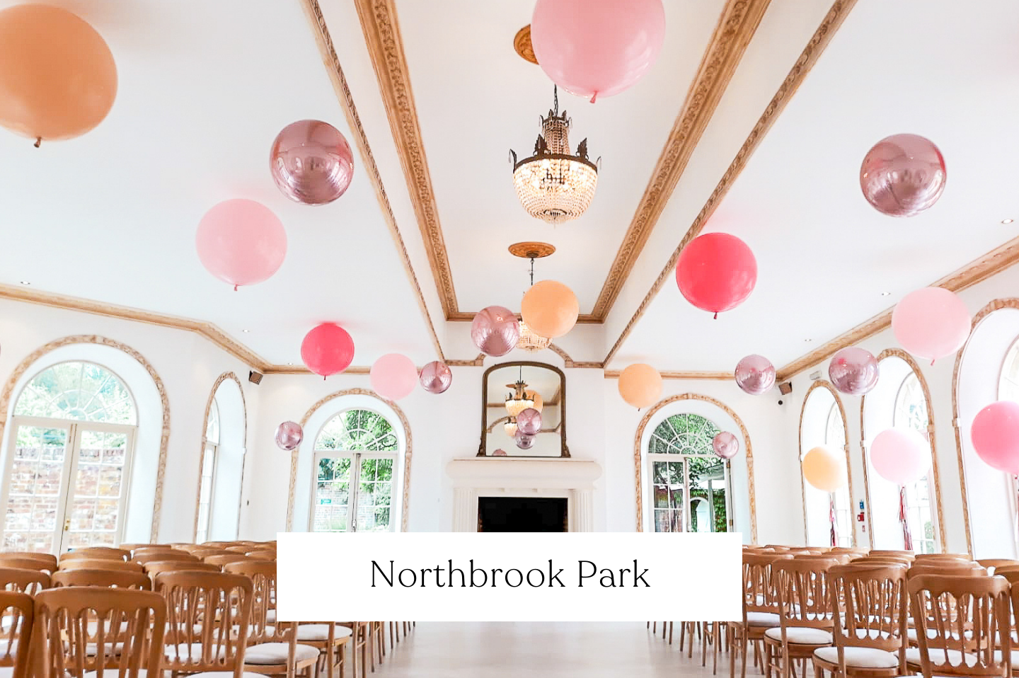 An elegant, spacious wedding venue with a high ceiling decorated with pink, peach, and metallic balloons hanging from it. 