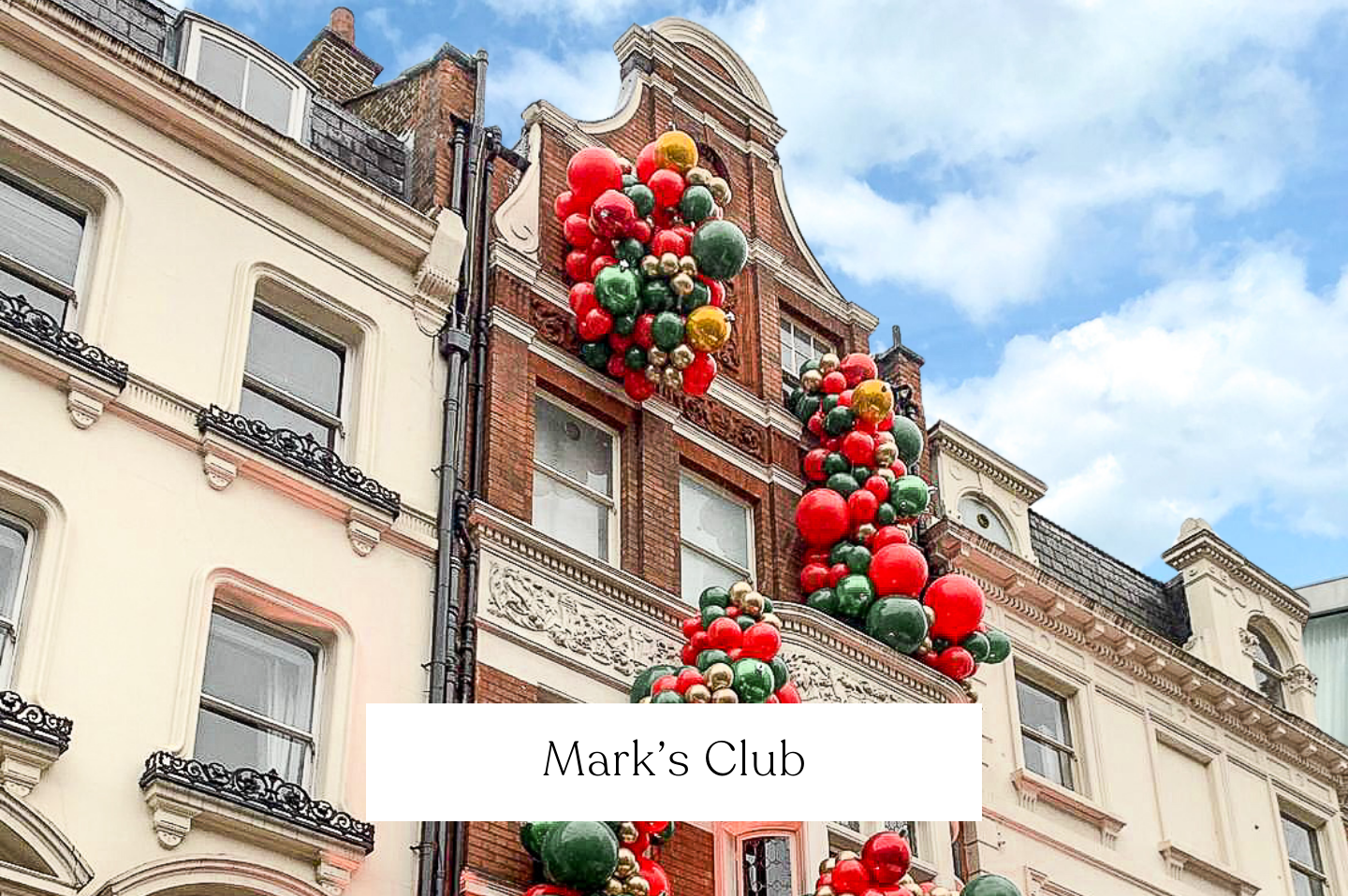 Decorative Christmas balloons in red, green, gold, and silver balls hanging on the facade of a Mark's Club, London.