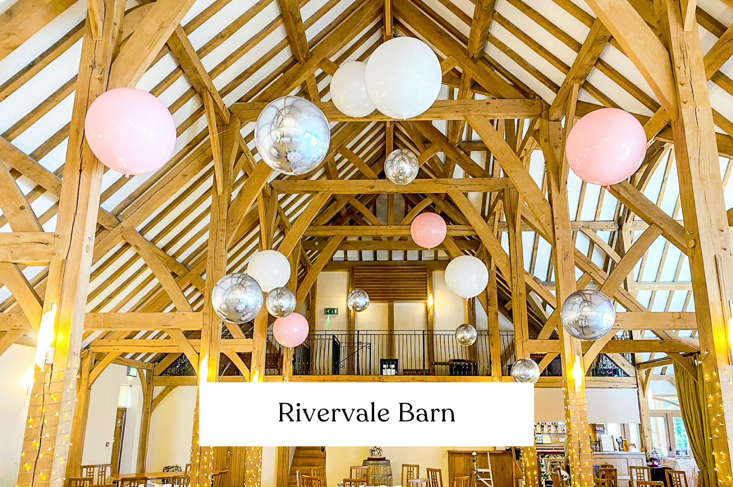 Interior of Rivervale Barn, Hampshire with wooden beams, hanging pink, white, and silver balloons, string lights, for a wedding reception. 