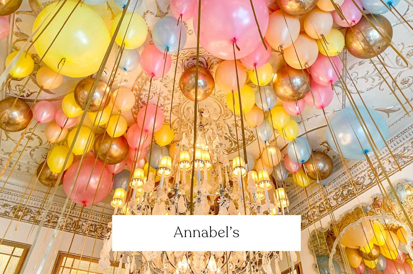 Ceiling decorated with numerous colorful balloons in pink, yellow, blue, gold, and silver, with some balloons attached to long ribbons hanging down.  Annabel's London.