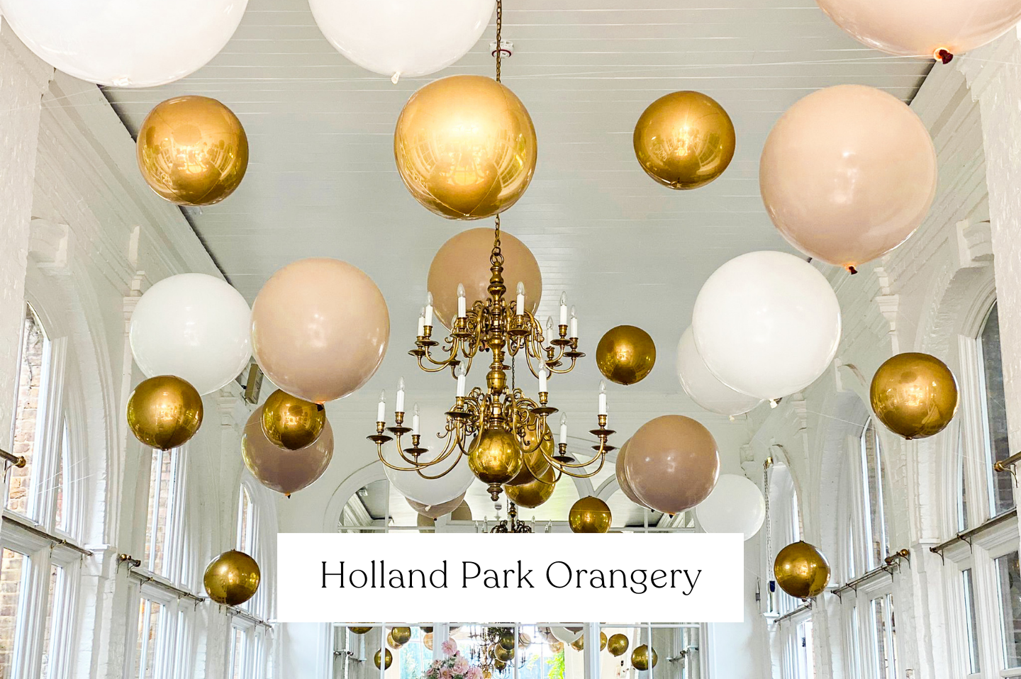 Decorative wedding balloons and chandeliers hanging from the ceiling of a light-filled conservatory or event space.