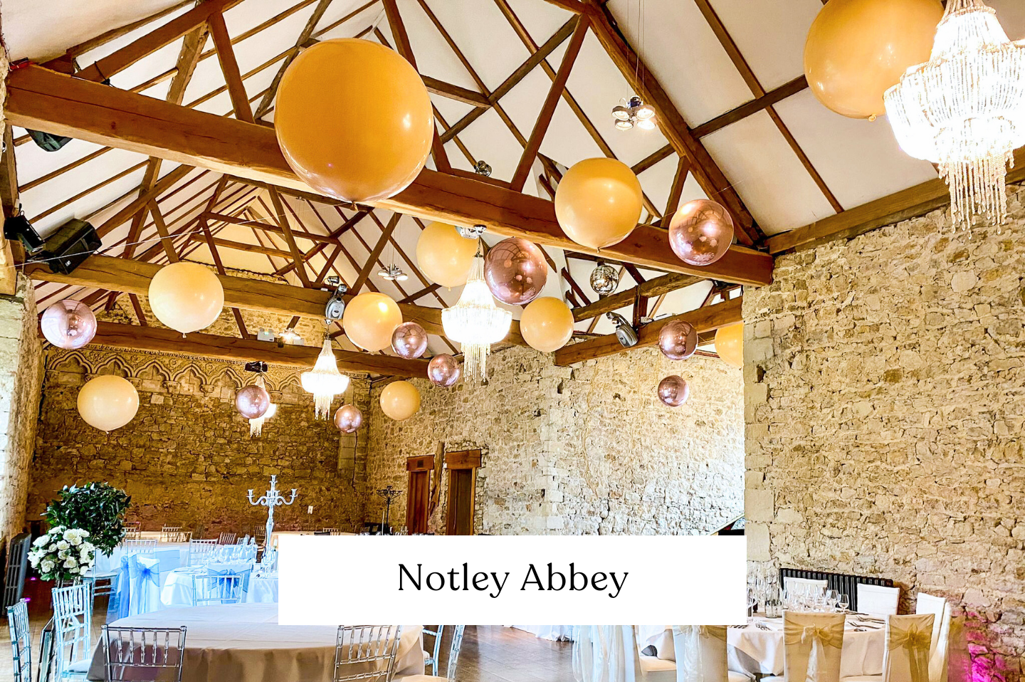 Interior of a rustic venue space decorated for a celebration with suspended balloon ceiling in gold, white, rose gold for a wedding. 