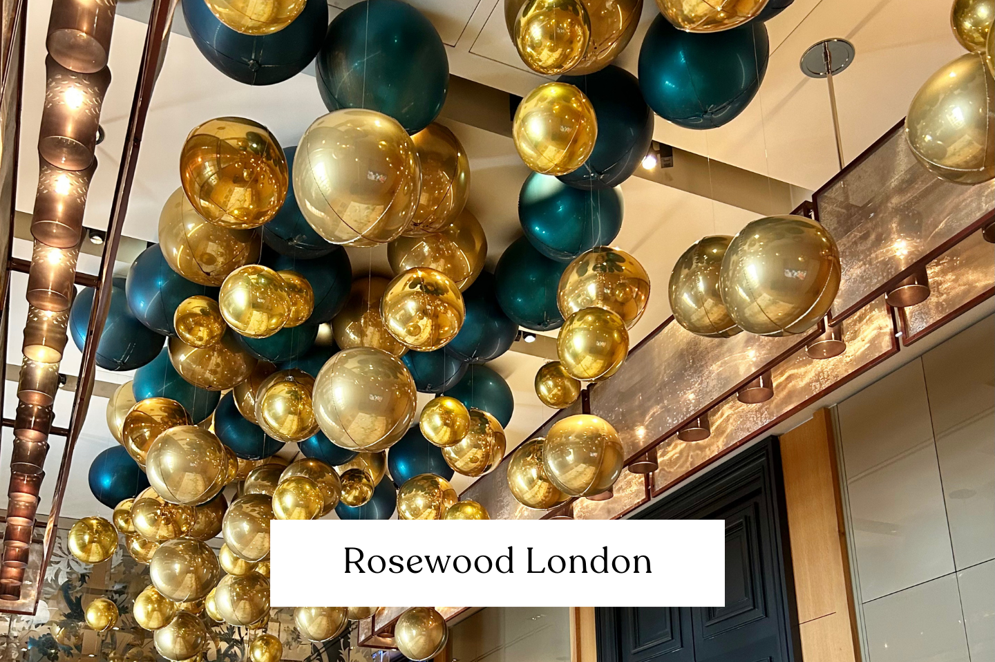 Decorative ceiling installation of gold and dark teal balloons orb lines hanging from the ceiling in a luxurious interior space at Rosewood London.