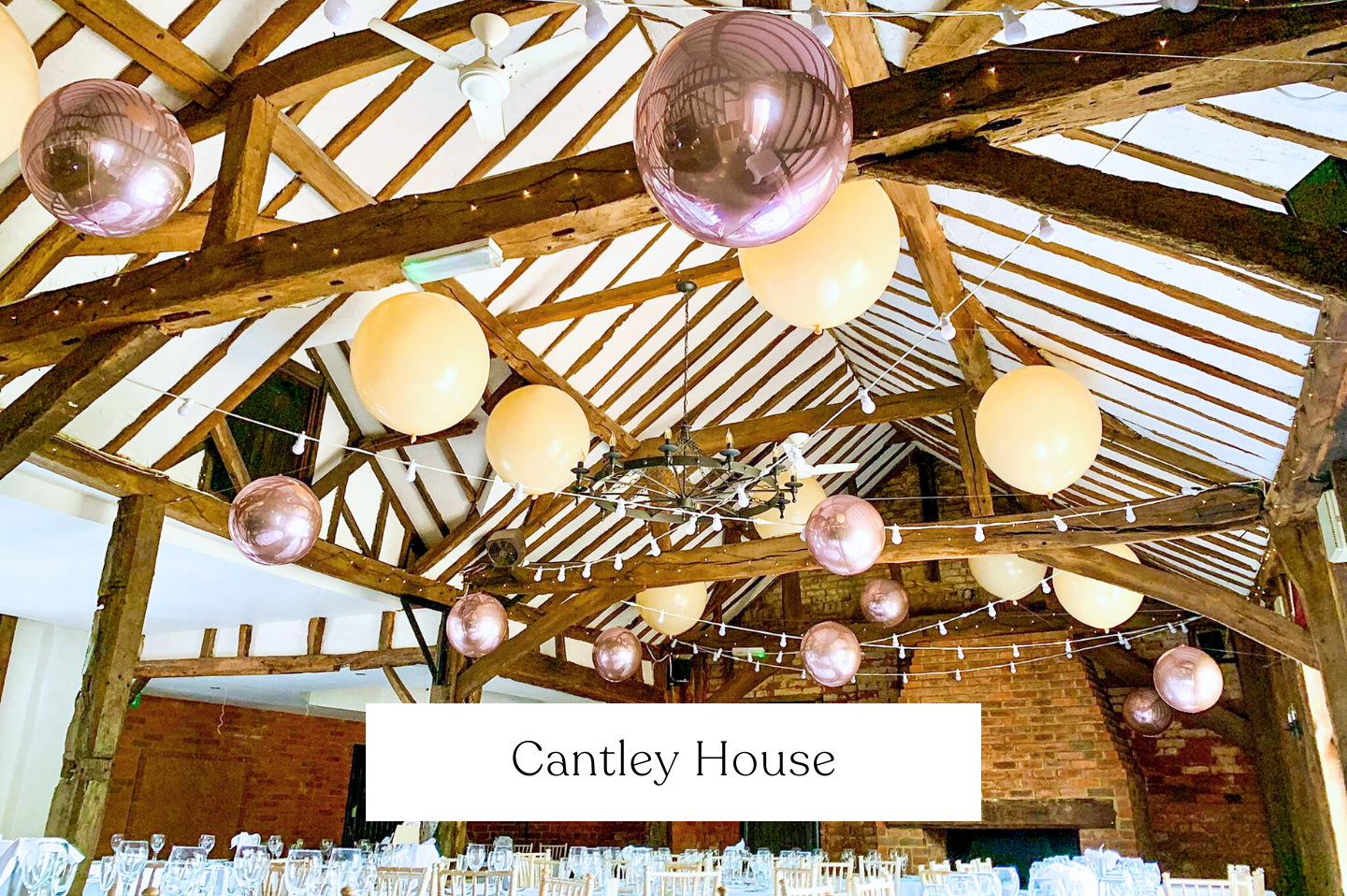 Decorated indoor wedding event space at Cantley House with exposed wooden beams, hanging pink and cream round lanterns, string lights, and a brick fireplace.