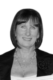 Black and white photograph of a smiling woman with shoulder-length hair, wearing a dark blazer and a necklace.