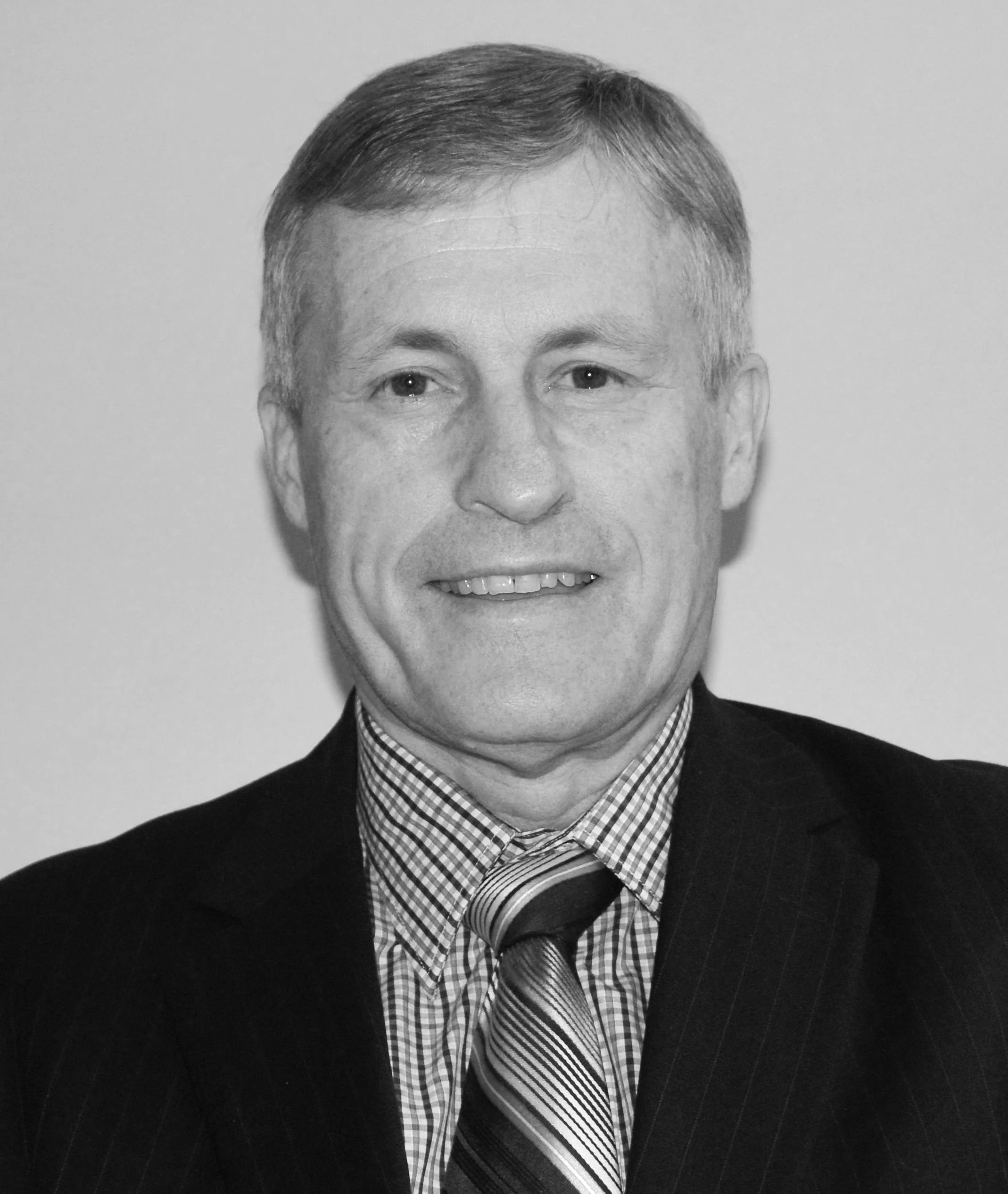 Black and white photo of a middle-aged man in a suit and striped tie, smiling with short hair, against a plain background.