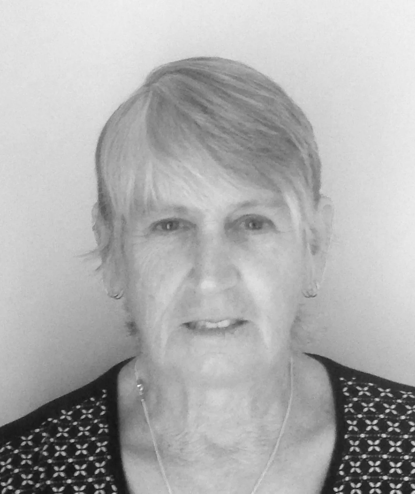 Black and white photo of an elderly woman with short hair, wearing earrings and a necklace, making an expressive face.