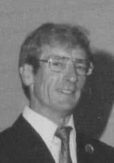 Black and white photo of a smiling man wearing glasses, a suit, and a tie.