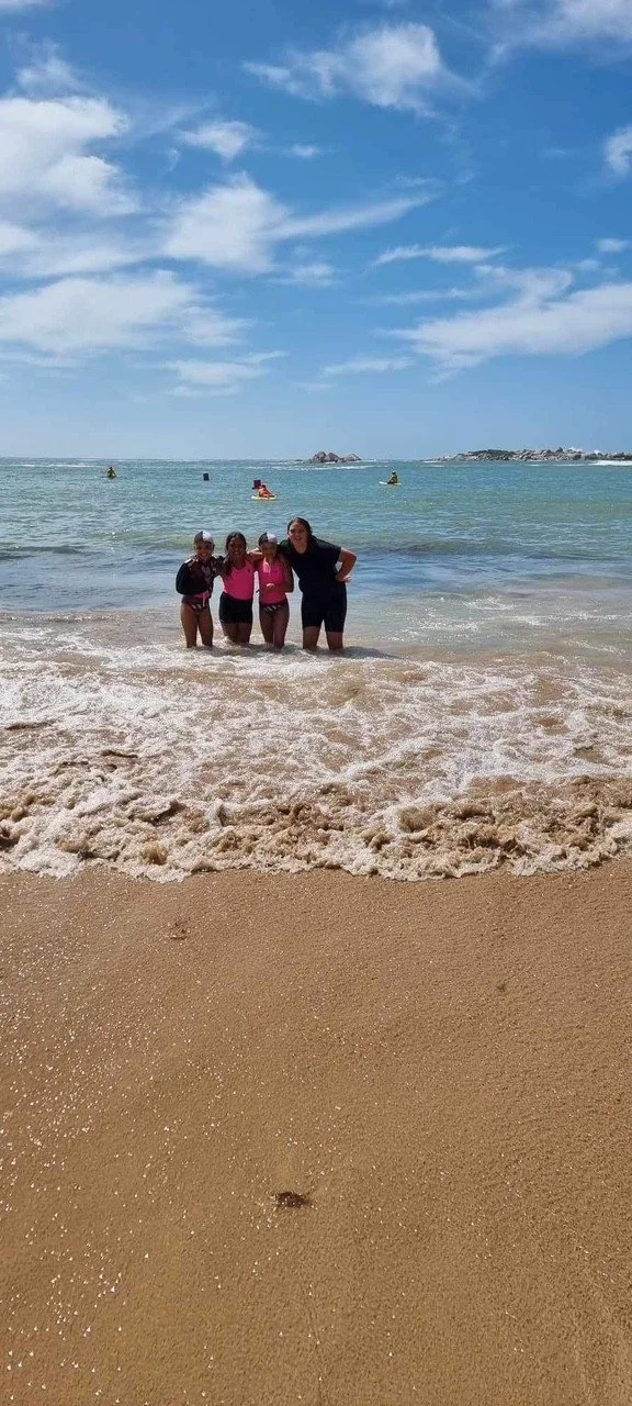 Group of four people standing at the shoreline on a beach with the ocean and a blue sky in the background.