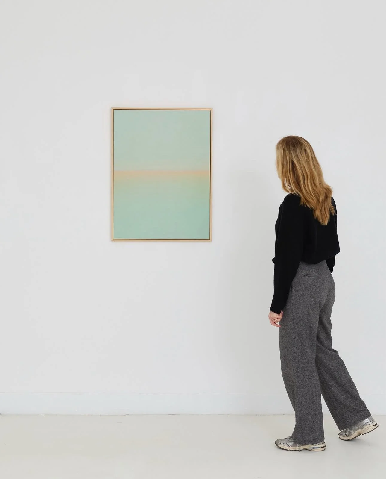 Een vrouw kijkt naar een abstract schilderij in een witte kunstgalerij.