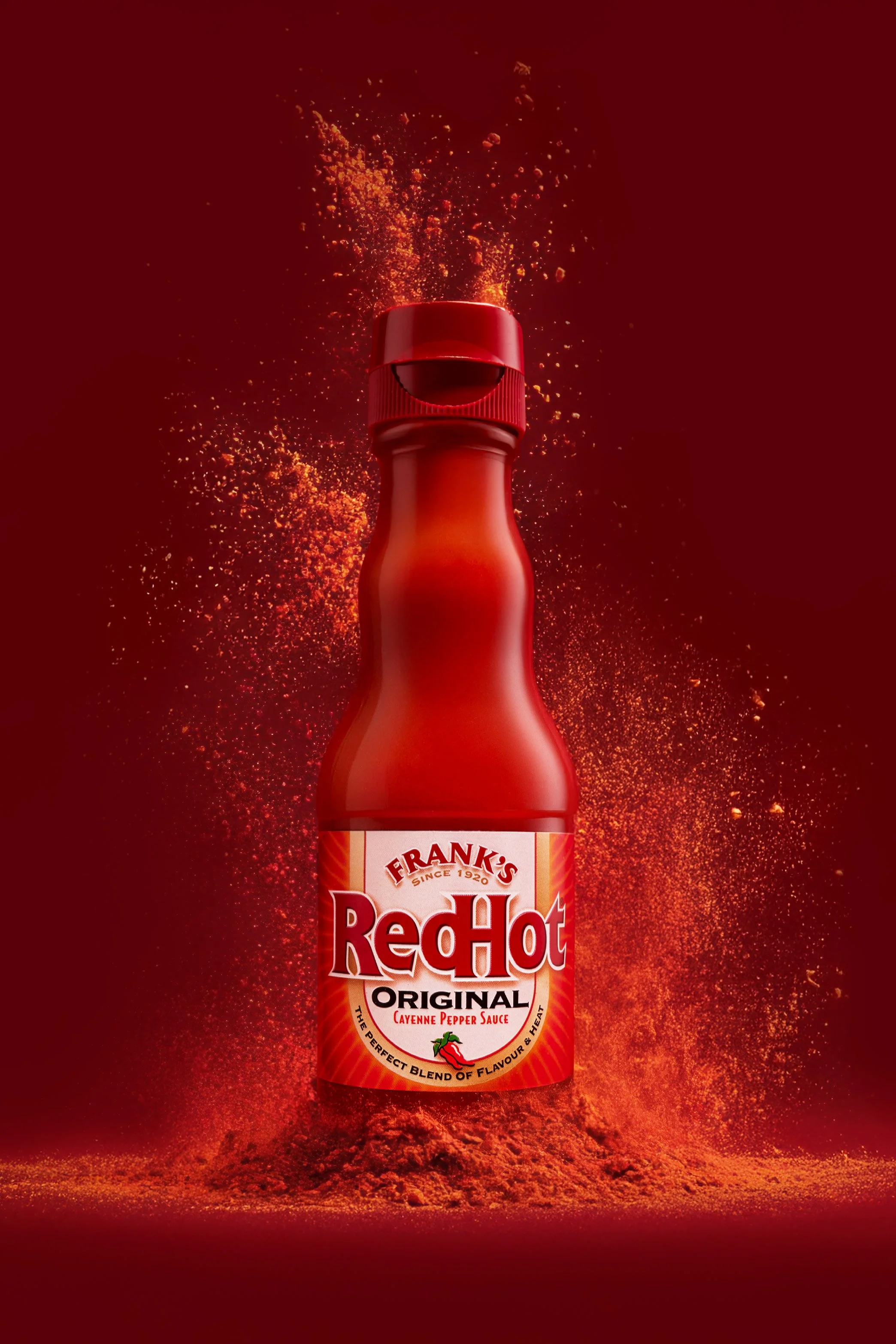 This image is of franks red hot sauce with an explosion of hot fiery cayenne pepper, chilli sauce, red background