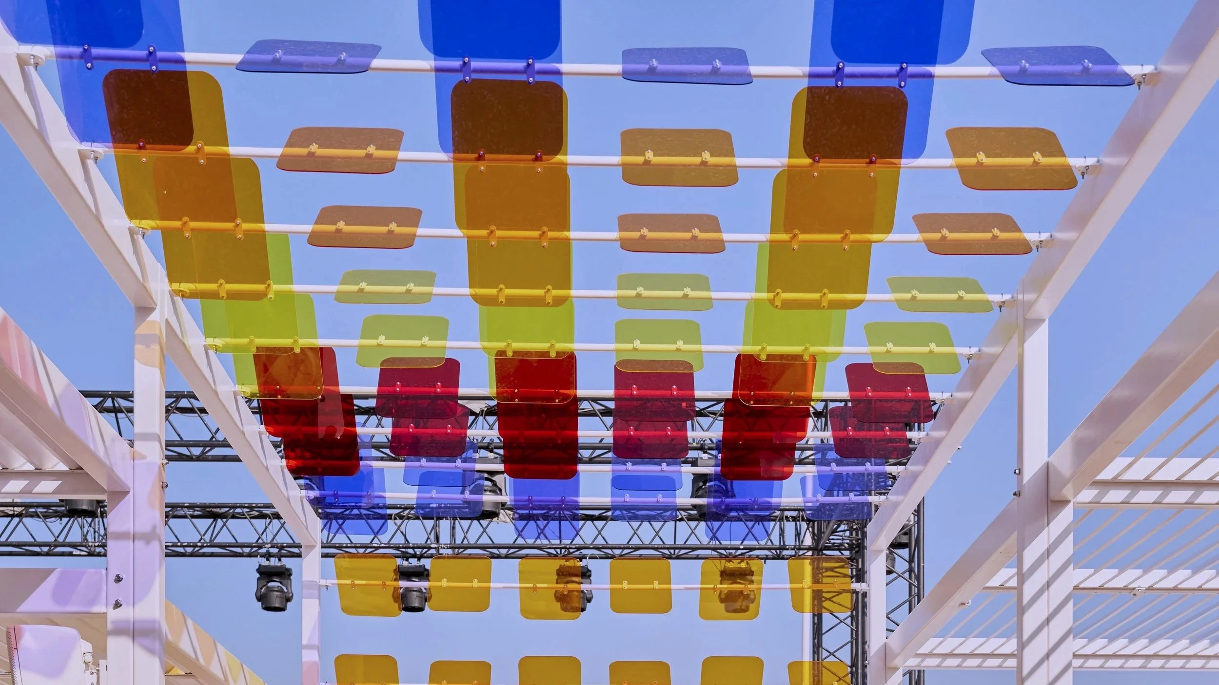 Colorful plastic panels in red, yellow, blue, and green arranged on a white outdoor structure against a clear blue sky.