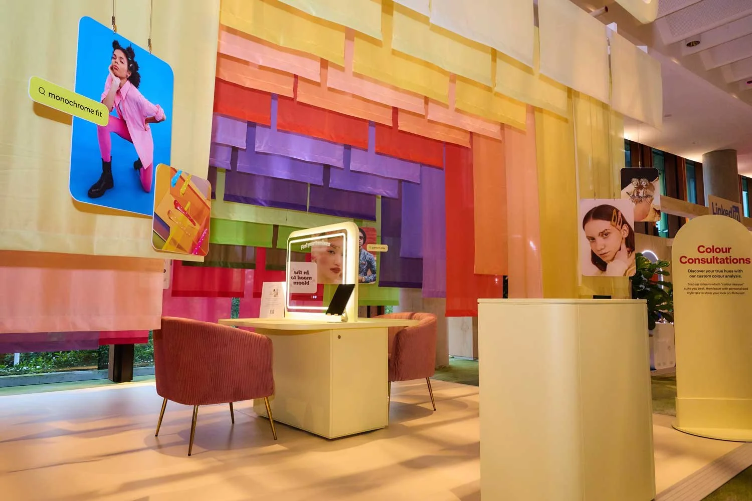 Interior of a colorful style reading zone for Pinterest at Cairns Crocs advertiser event with a rainbow-colored backdrop and posters of women's faces, a sign reading 'Colour Consultations,' a mirror with lights, and seating area with pink chairs.